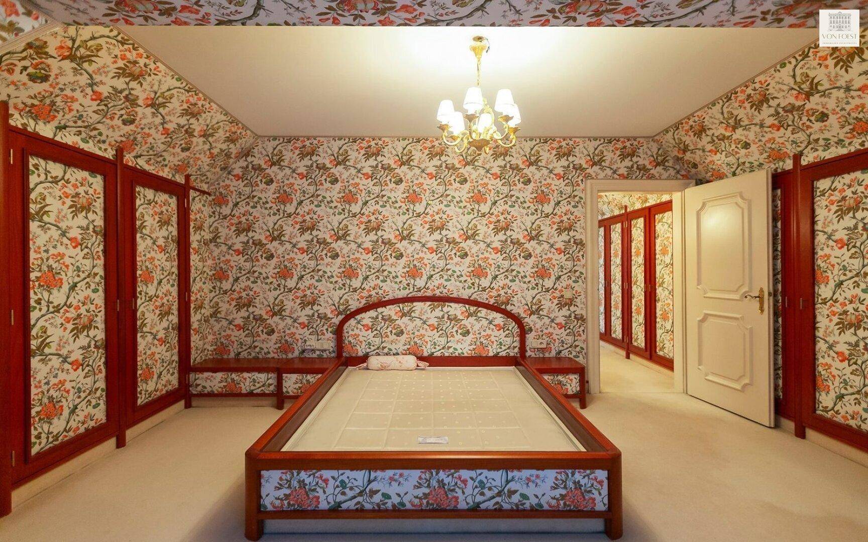 Schlafzimmer mit auffälliger floraler Tapete, klassischem Holzbett und integrierten Kleiderschränken.