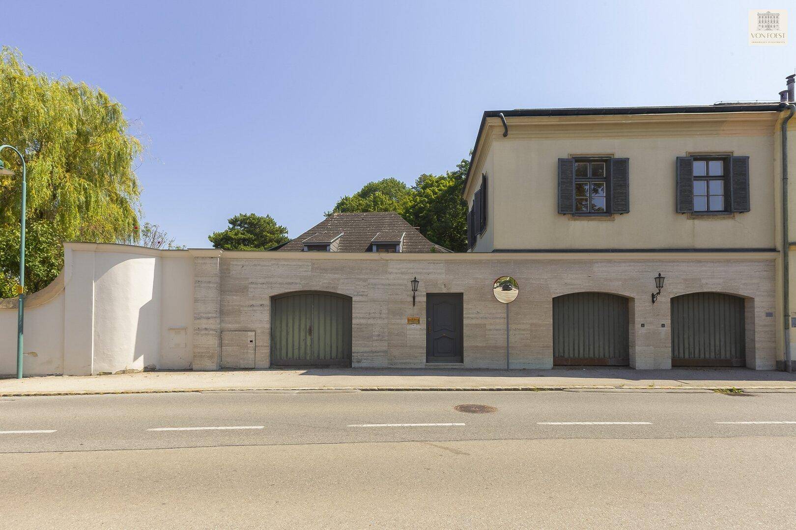 Historische Straßenfassade des Anwesens mit mehreren Garagentoren und einem eleganten Eingang.