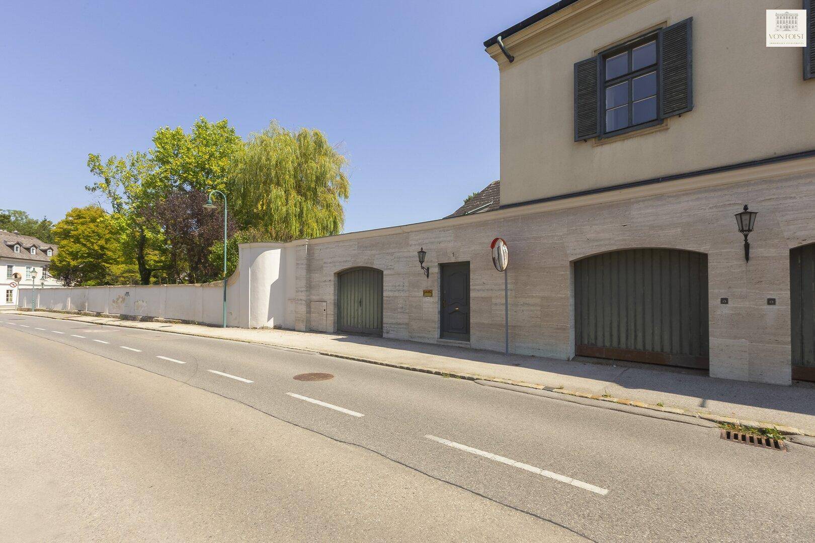 Ansicht der historischen Gebäudefassade von der Straße aus, mit gepflegter Steinmauer und Garagen.