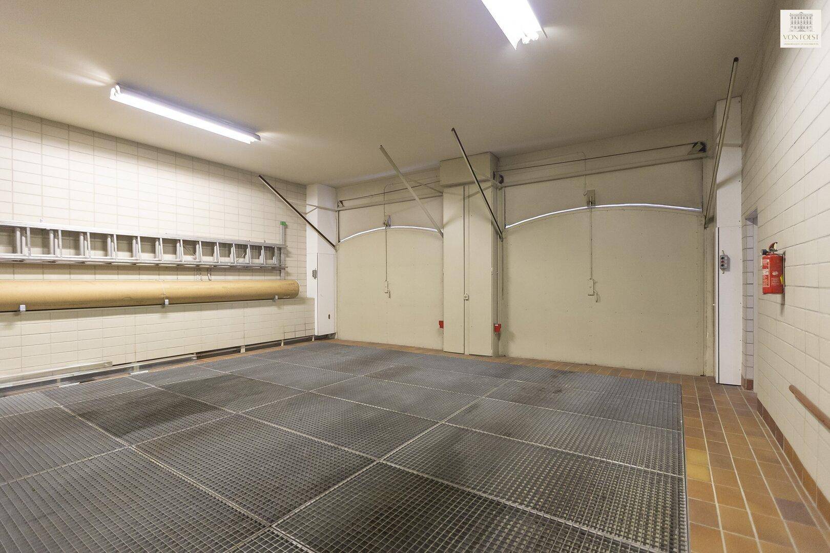 Geräumige Garage mit robustem Metallgitterboden und gefliesten Wänden, ideal für Fahrzeuge.