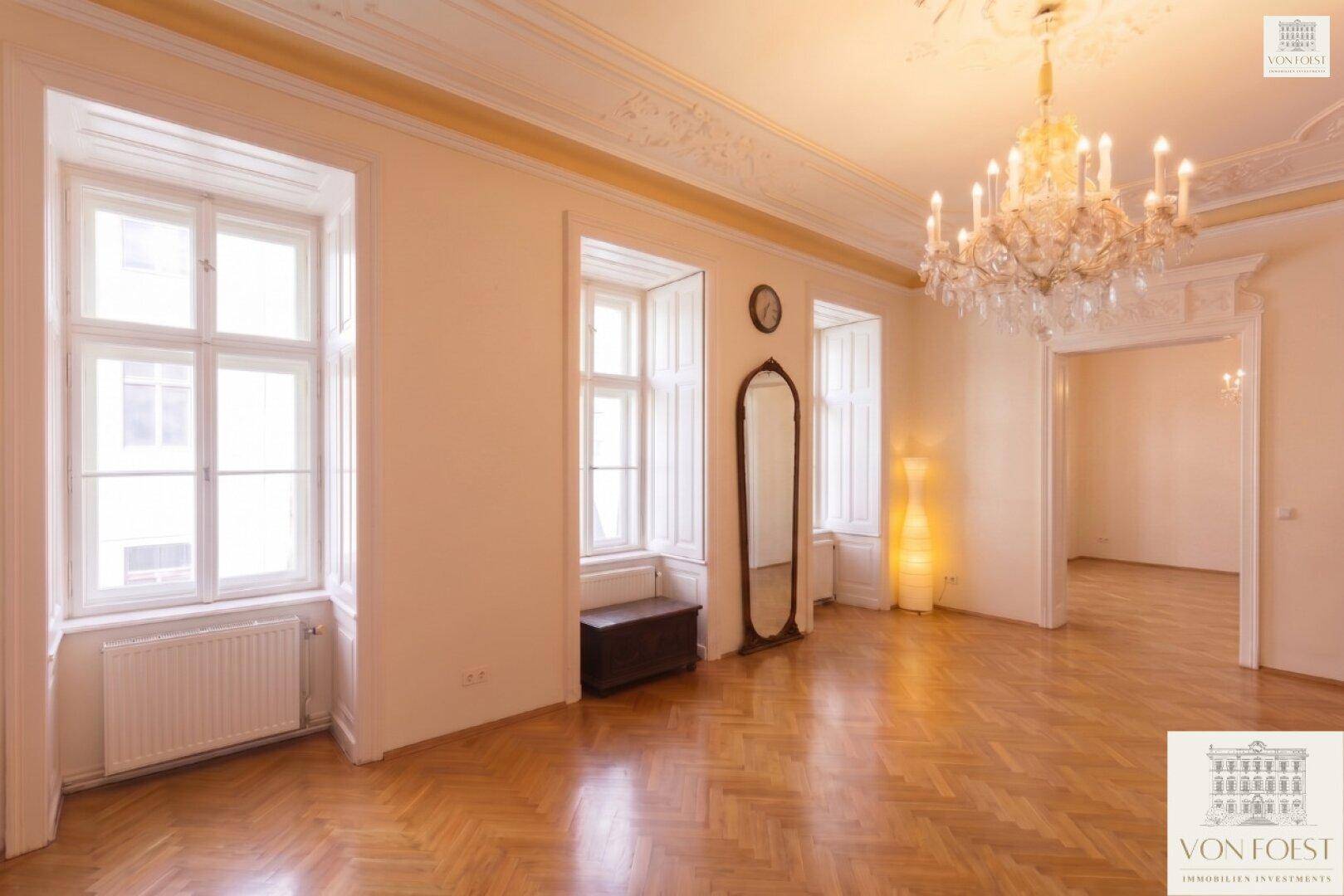 Geräumiges Zimmer mit Fischgrätparkett, Kronleuchter und großem Spiegel.