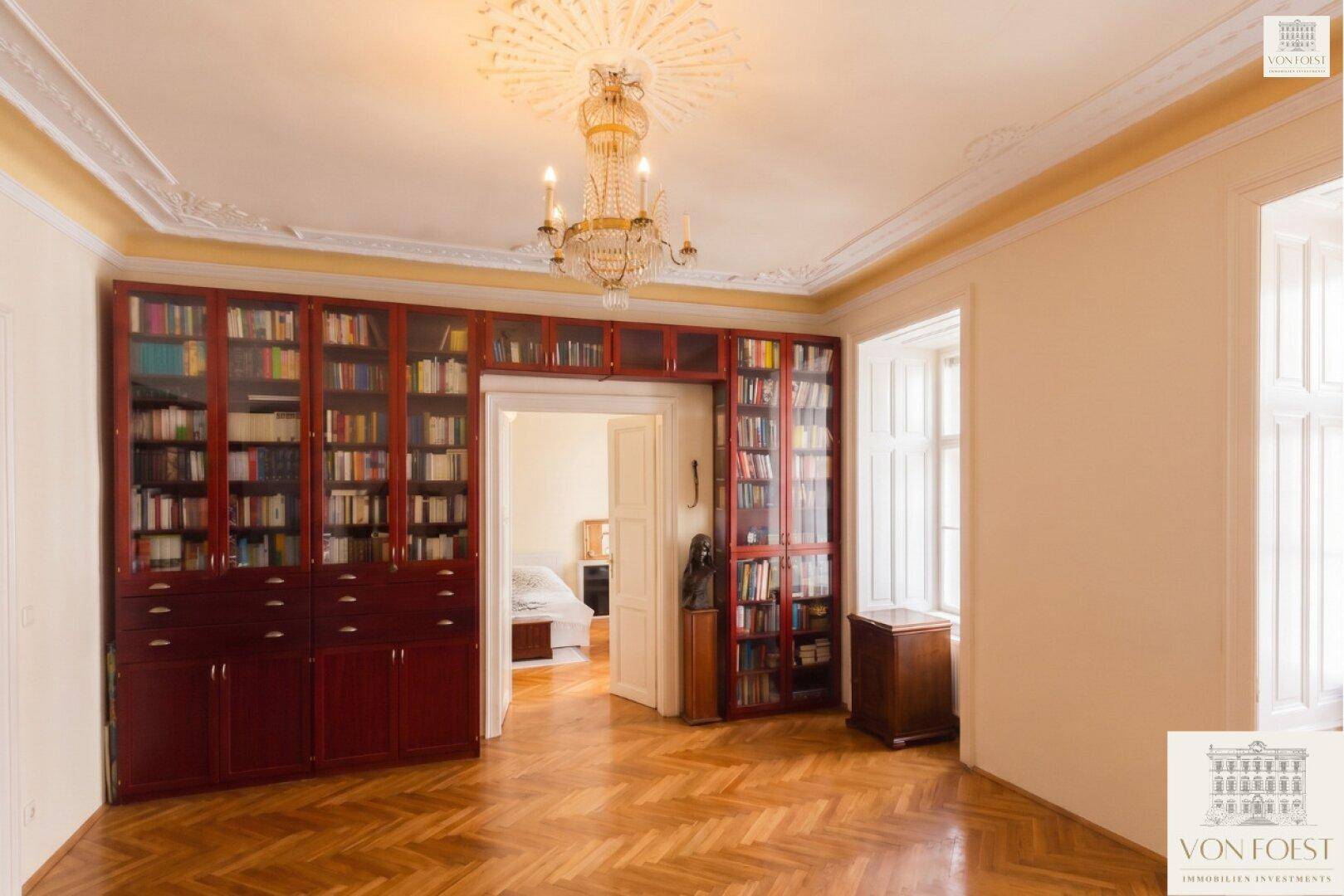 Zimmer mit großen, eingebauten Bücherregalen, Fischgrätparkett und Kronleuchter.