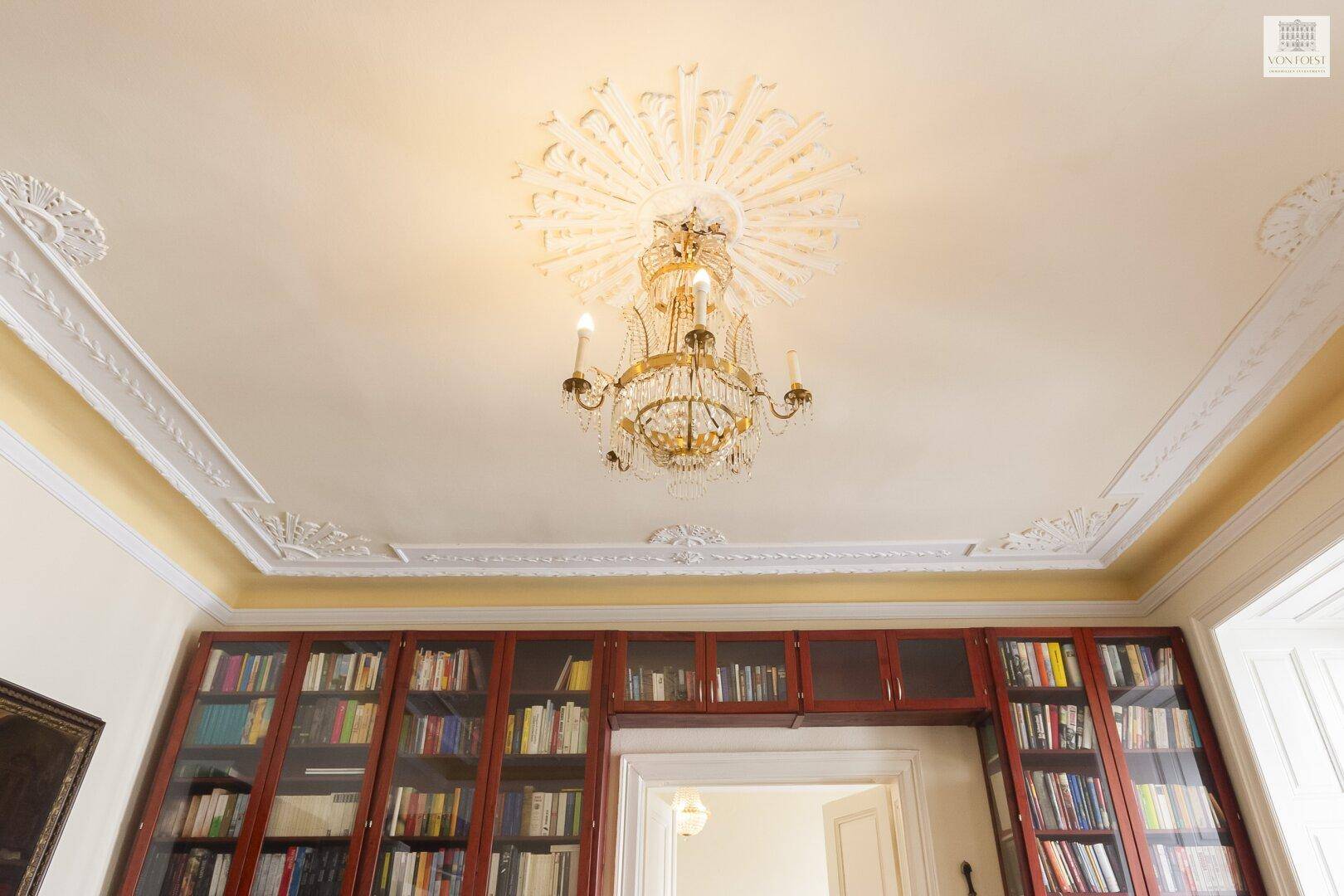 Detailaufnahme einer opulenten Stuckdecke mit Kronleuchter und goldener Verzierung.