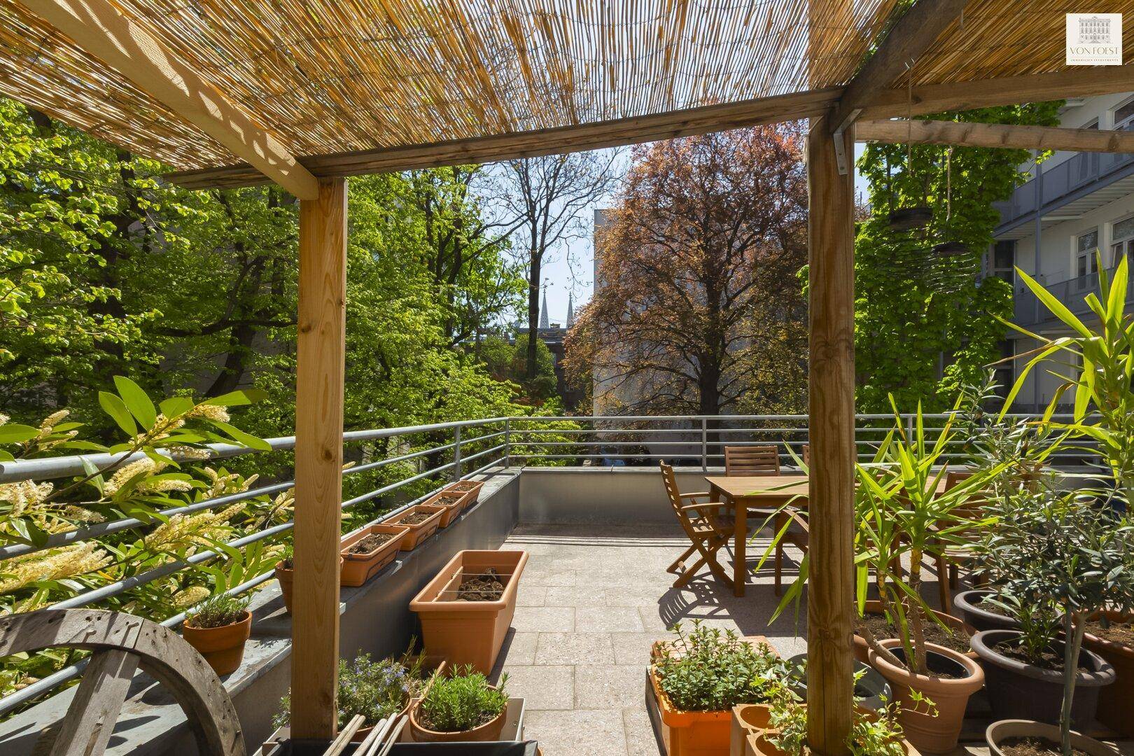 Sonnige Terrasse mit Bambusdach, Gartenmöbeln und üppiger Bepflanzung.