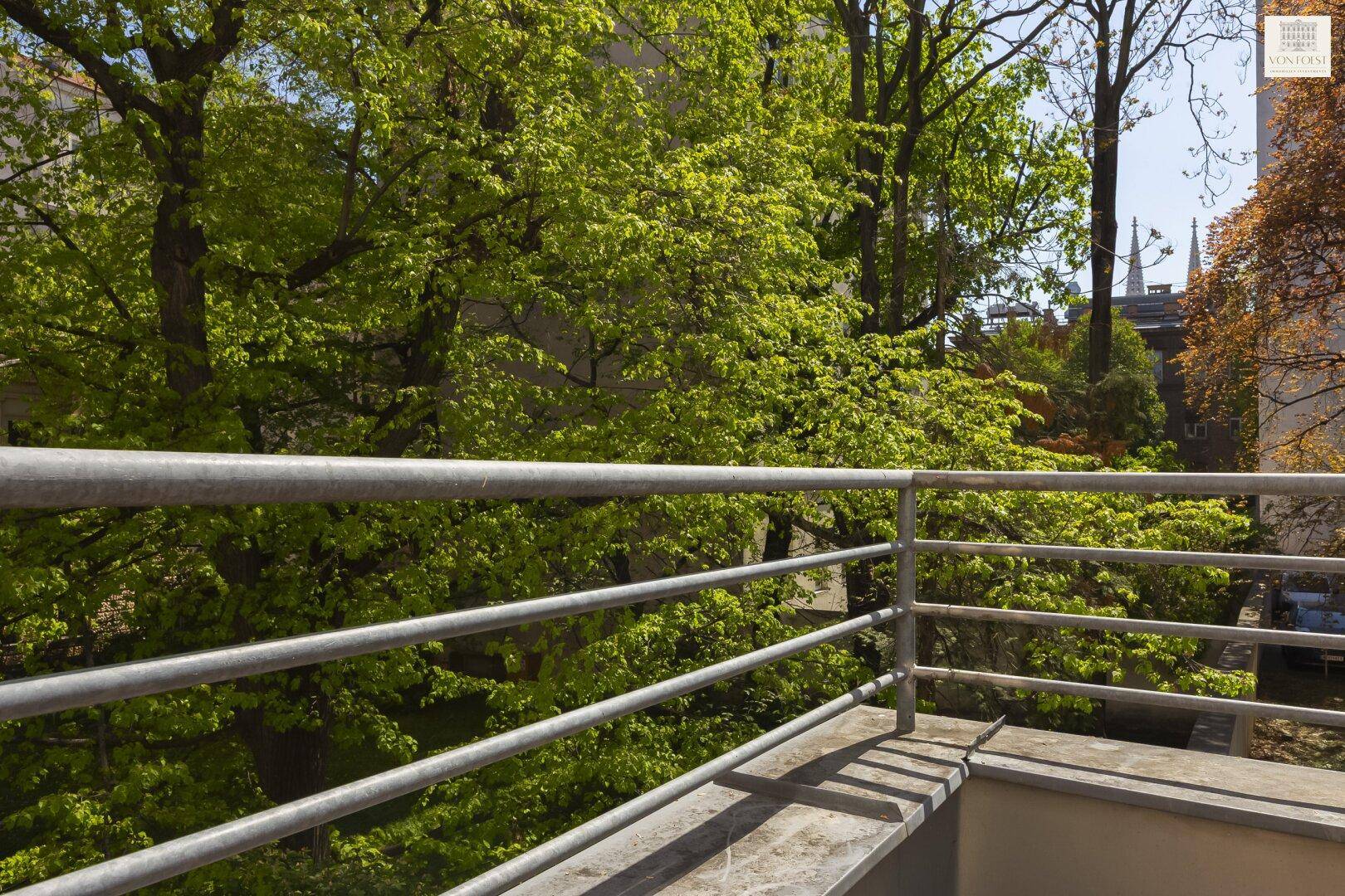 Balkon mit Metallgeländer und Blick auf grüne Bäume und die Umgebung.