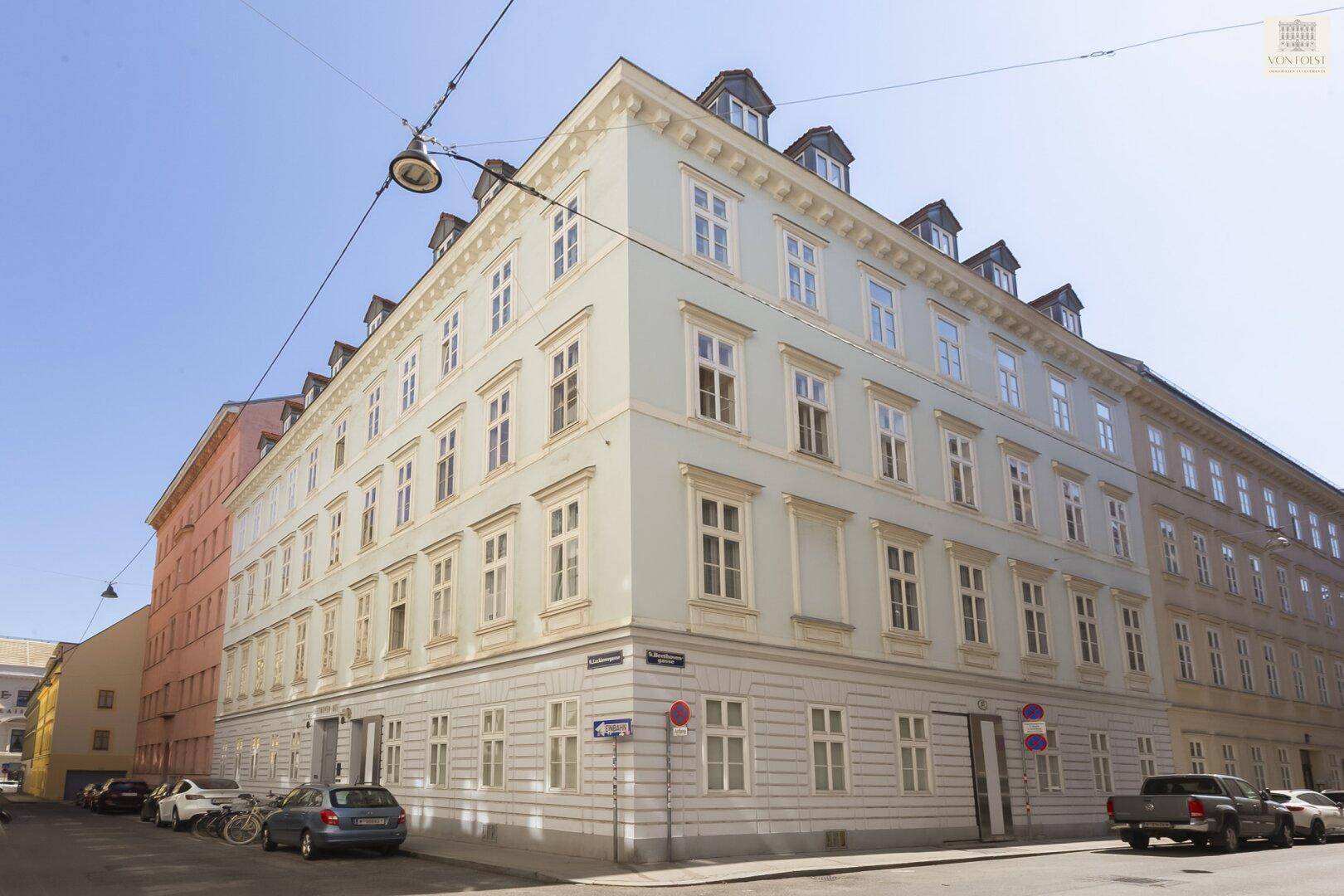 Eckgebäude mit klassischer Architektur, vielen Fenstern und Mansarddach in der Stadt.