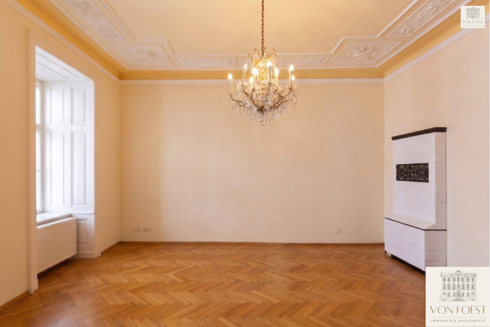 Geräumiges Zimmer mit Fischgrätparkett, Kachelofen und hohen Decken.