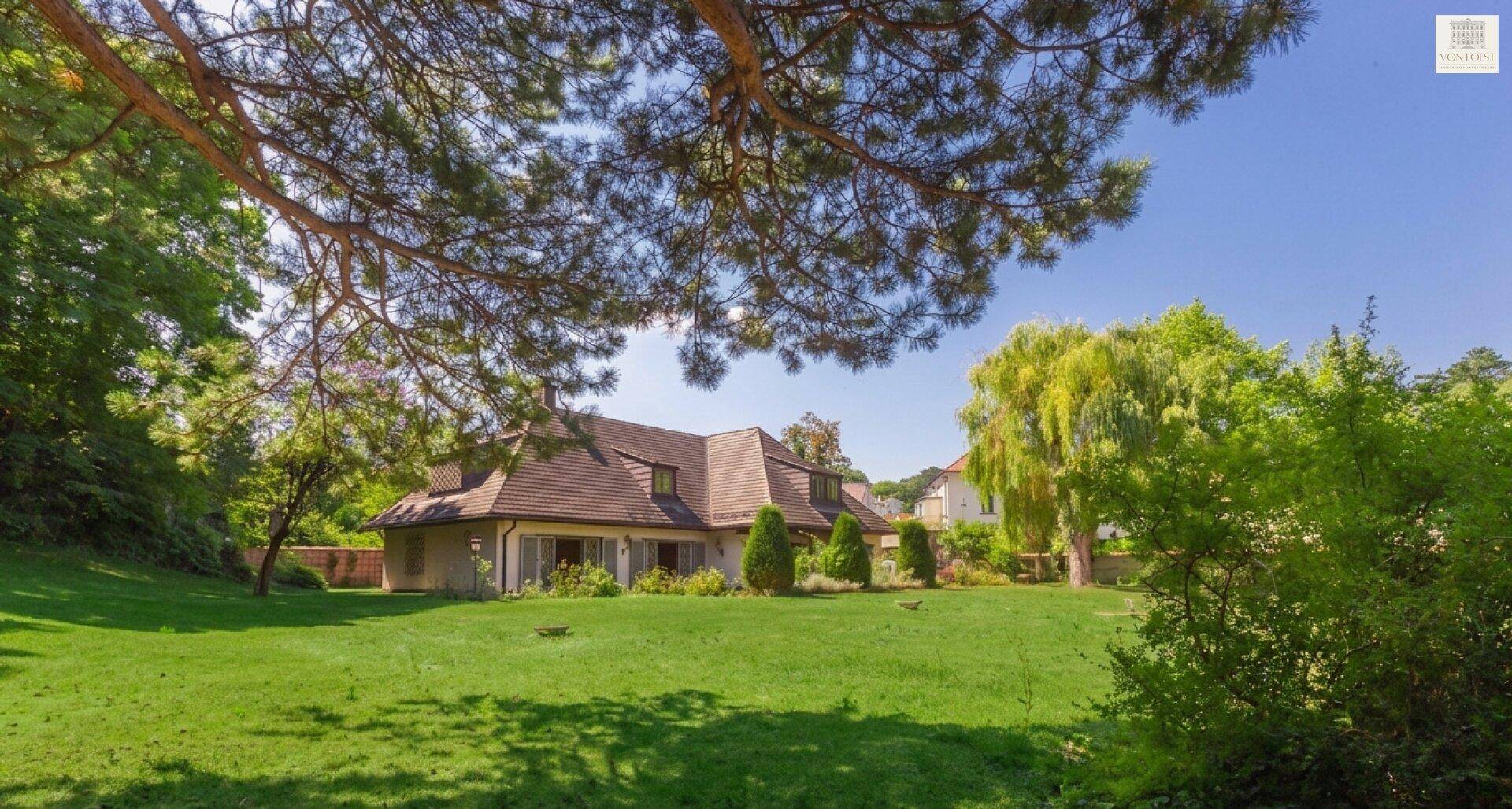 Weitläufiger Gartenbereich mit üppigem Grün und Blick auf das charmante Landhaus unter blauem Himmel.