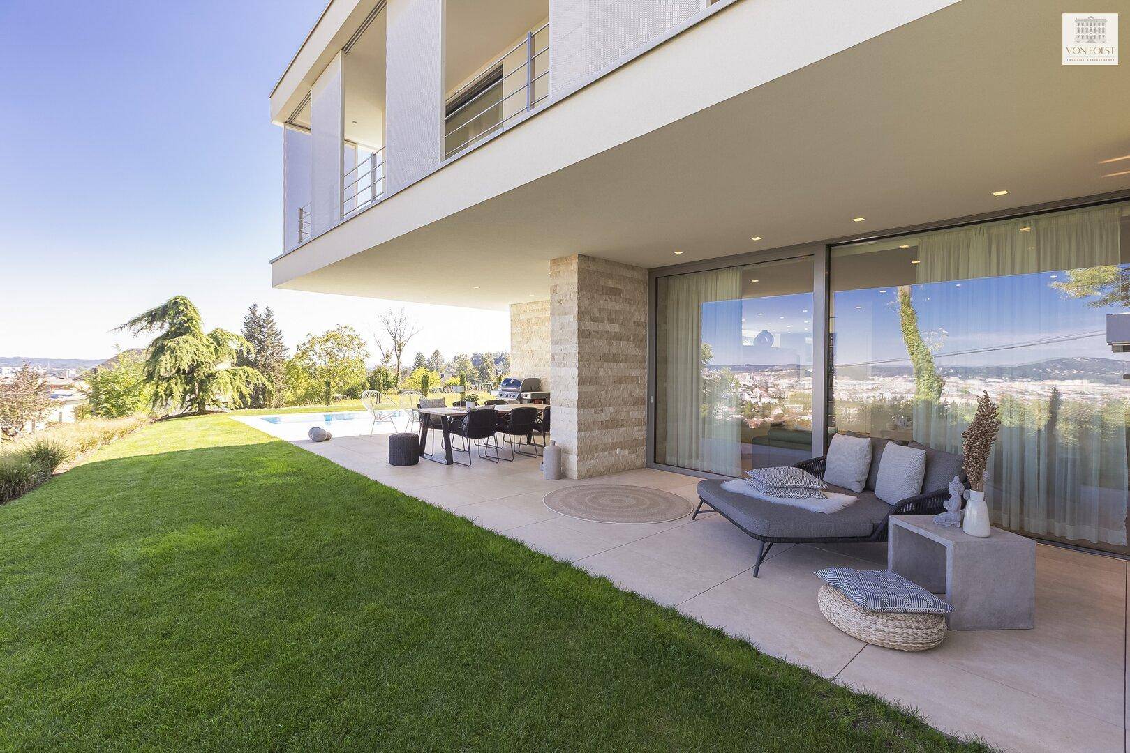 Geräumige Terrasse mit Essbereich und Lounge-Möbeln, angrenzend an den Pool und mit Stadtblick.