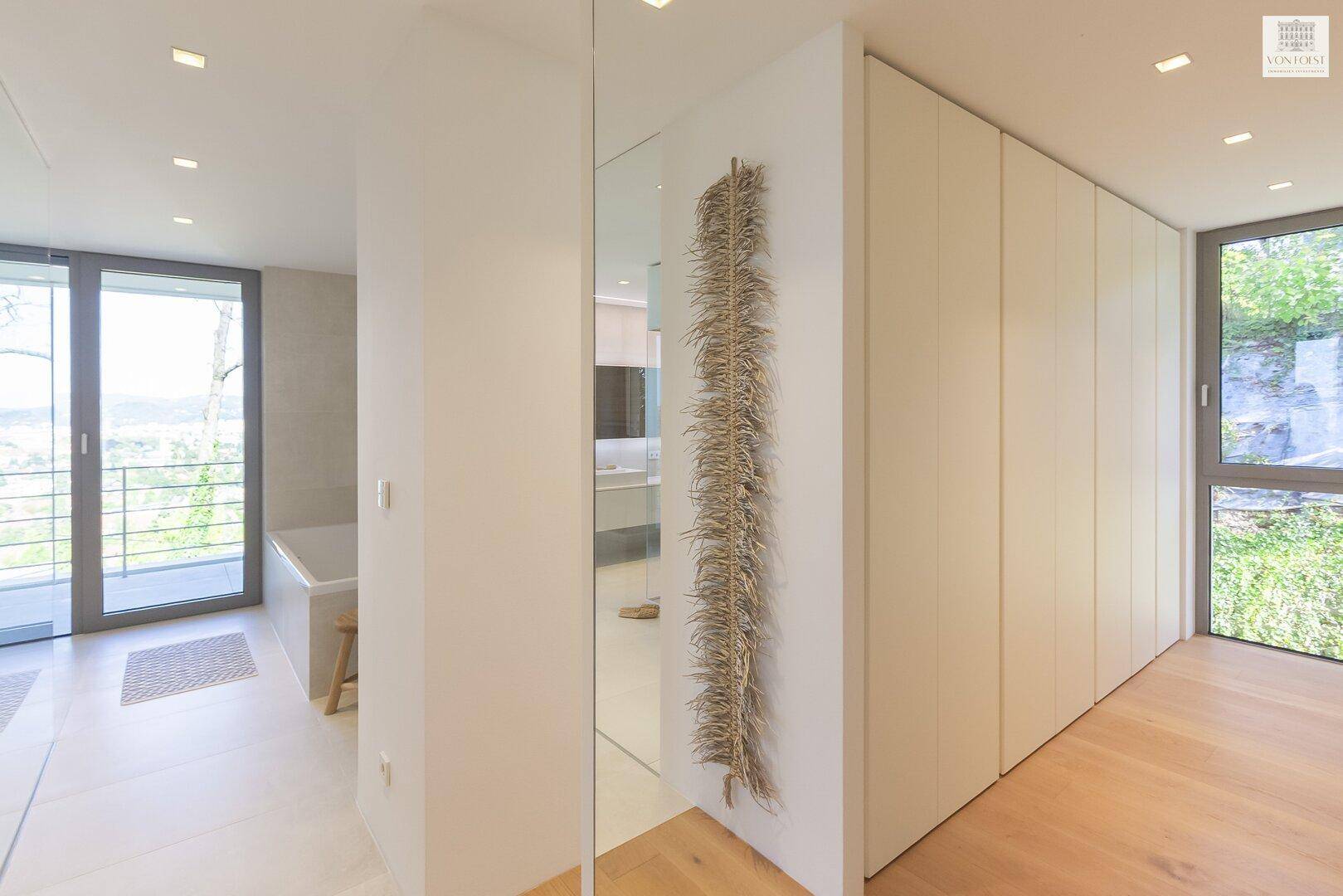 Heller Flur mit Einbauschränken und Holzboden, der zu einem Badezimmer mit Balkonzugang führt.