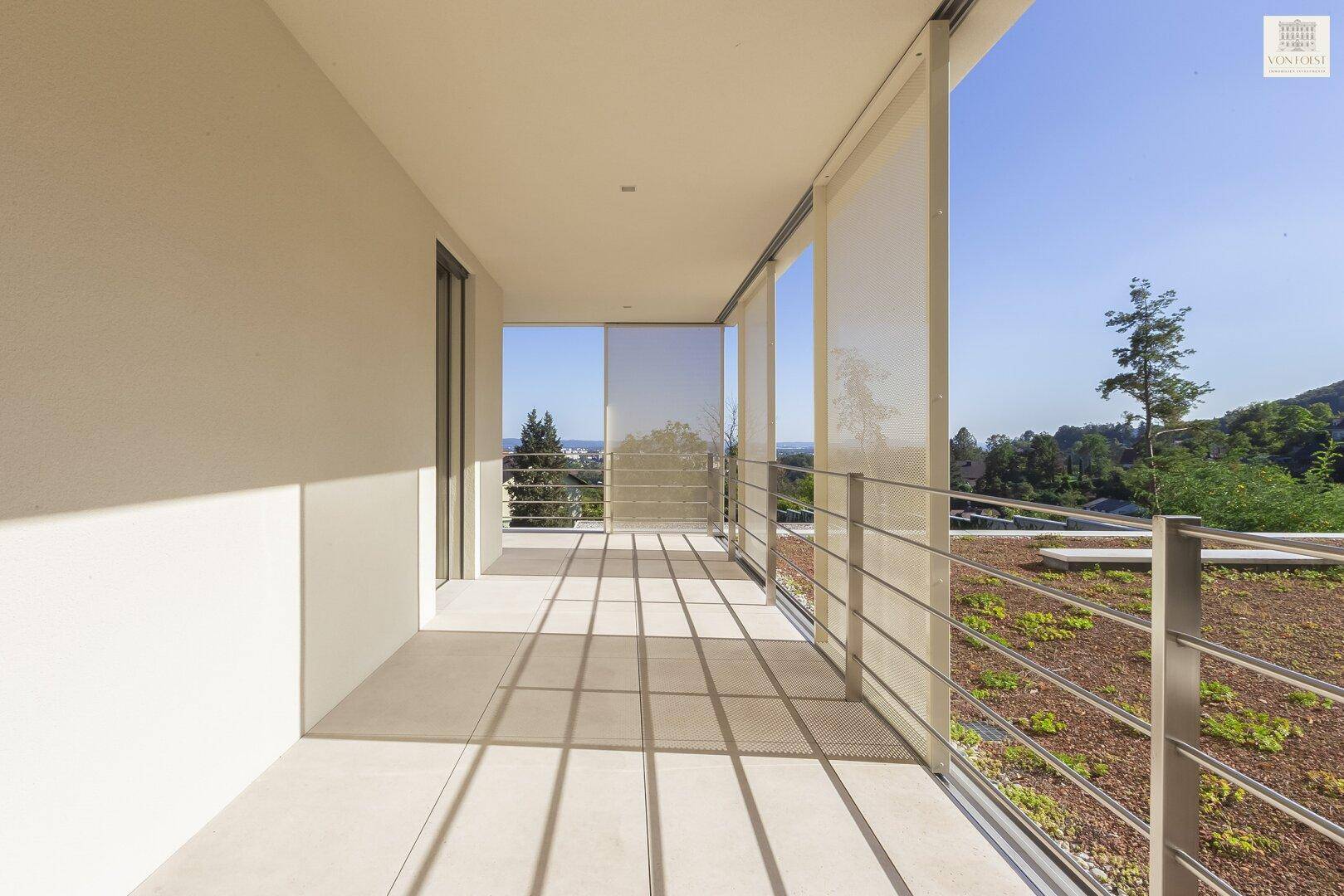 Überdachte Loggia mit Fliesenboden und Blick auf die grüne Umgebung und den Himmel.