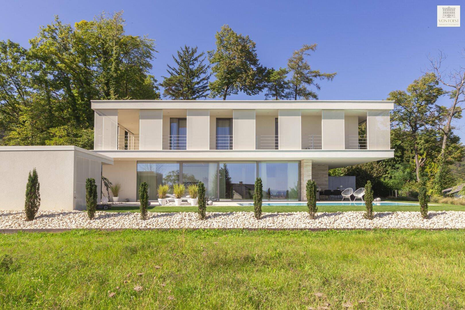 Elegante moderne Hausfassade mit großen Fenstern, Balkonen und einem gepflegten Gartenbereich mit Pool.