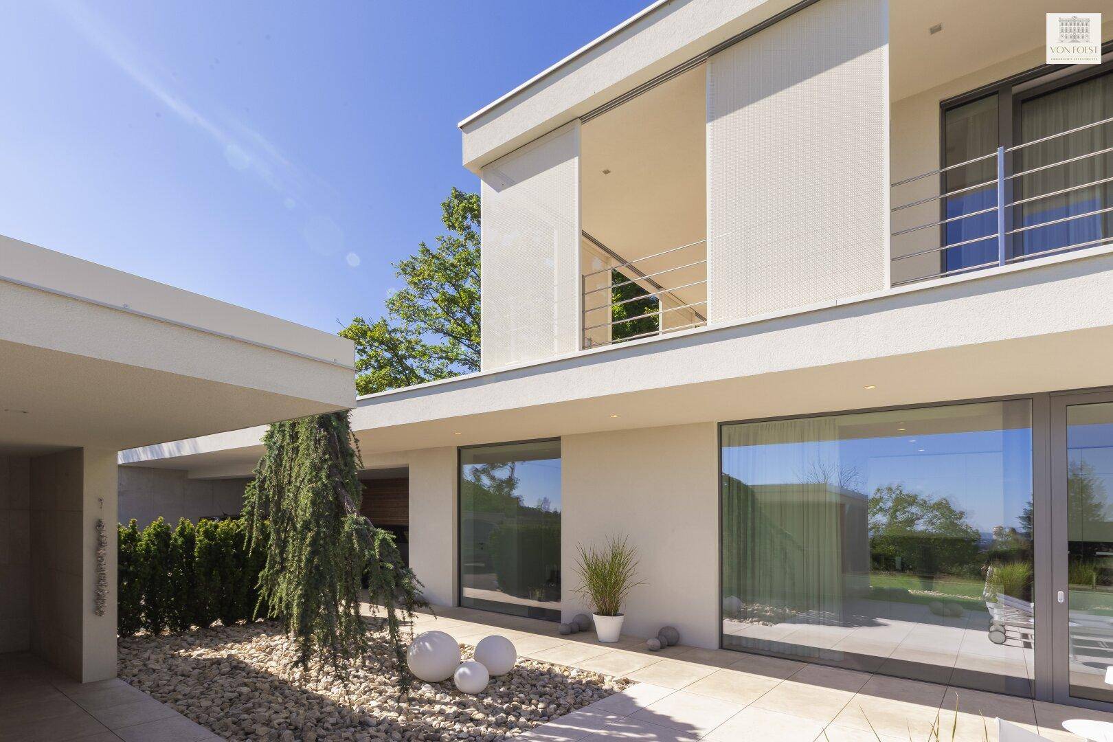 Seitenansicht des modernen Hauses mit großen Glasfronten und einem stilvollen Kieshof mit Zierbaum.