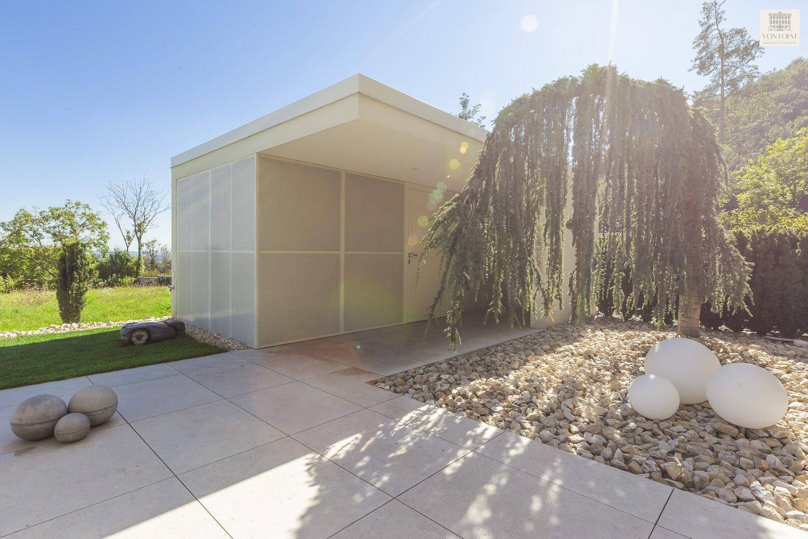 Moderner Gartenschuppen neben einem Kiesgarten mit Zierbaum und dekorativen Kugeln.
