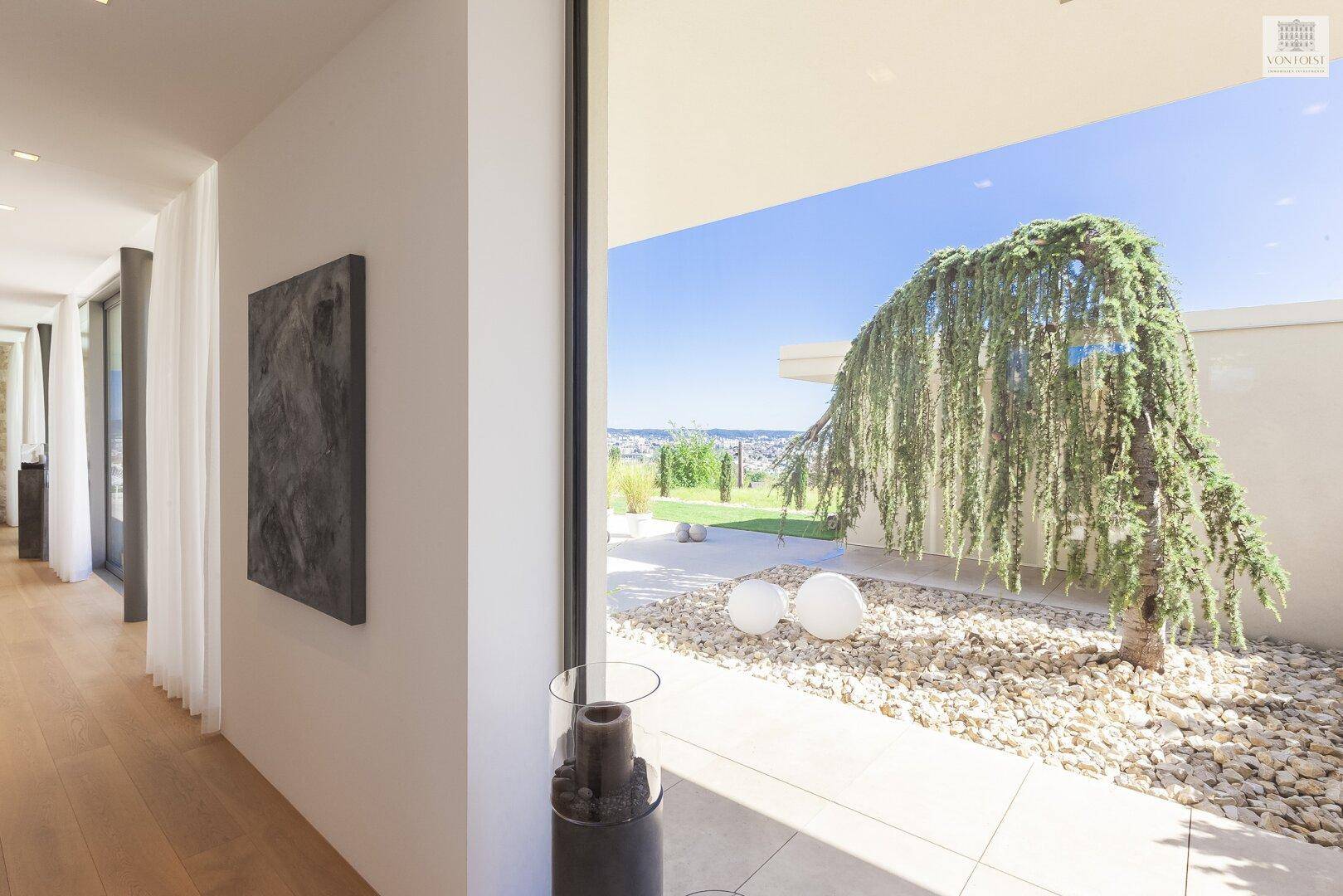 Heller Flur mit Holzboden und großem Fenster, das den Blick auf einen modernen Kiesgarten freigibt.