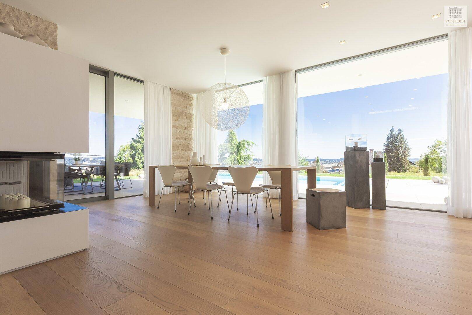 Heller Essbereich mit Holztisch, modernen Stühlen und großen Fenstern mit Poolblick.