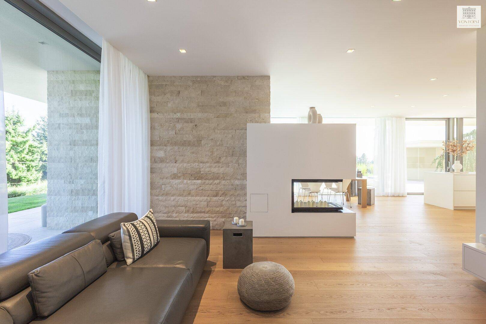 Modernes Wohnzimmer mit Ledersofa, Kamin und Holzboden, offen zum Essbereich.