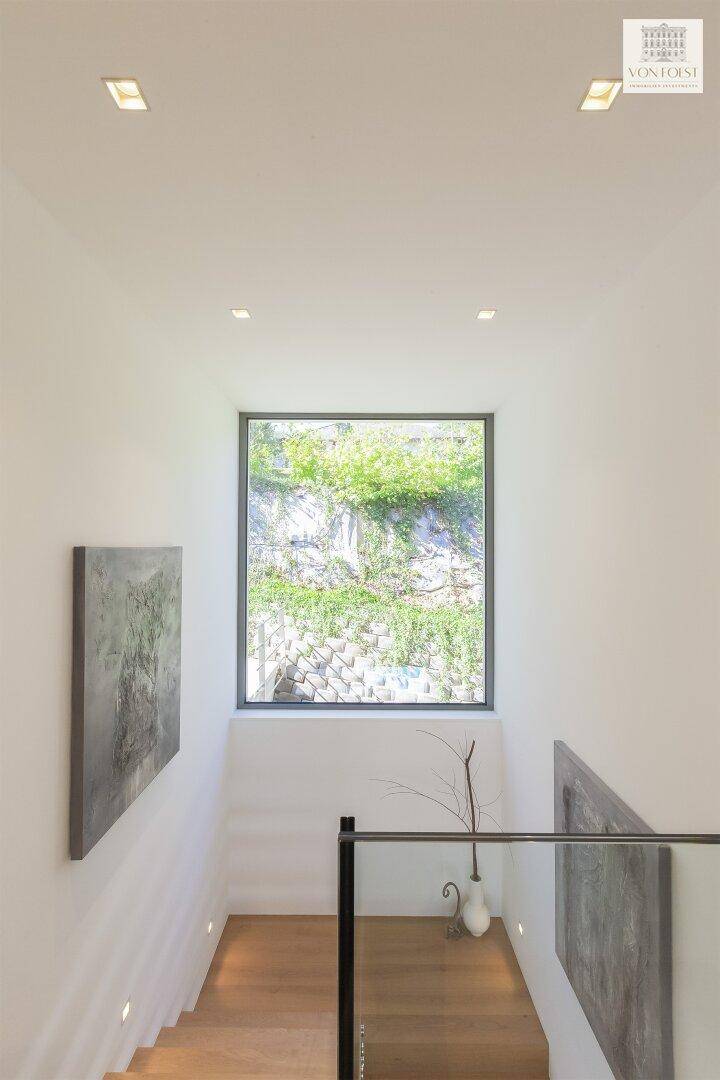 Moderne Treppe mit Holzstufen und Glasgeländer, die einen Blick auf eine begrünte Felswand bietet.