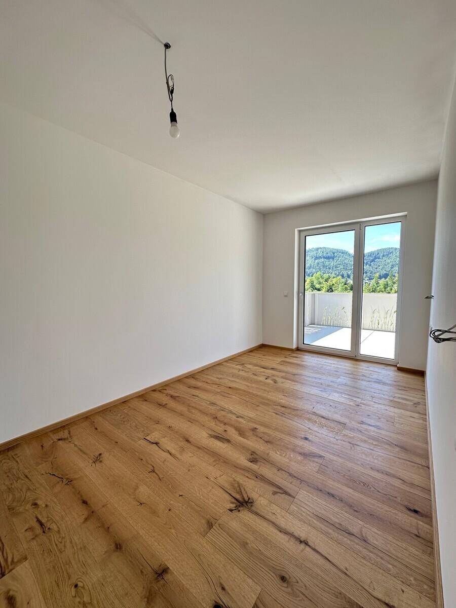 Leeres Zimmer mit Holzboden und großen Schiebetüren, die auf eine Terrasse führen.