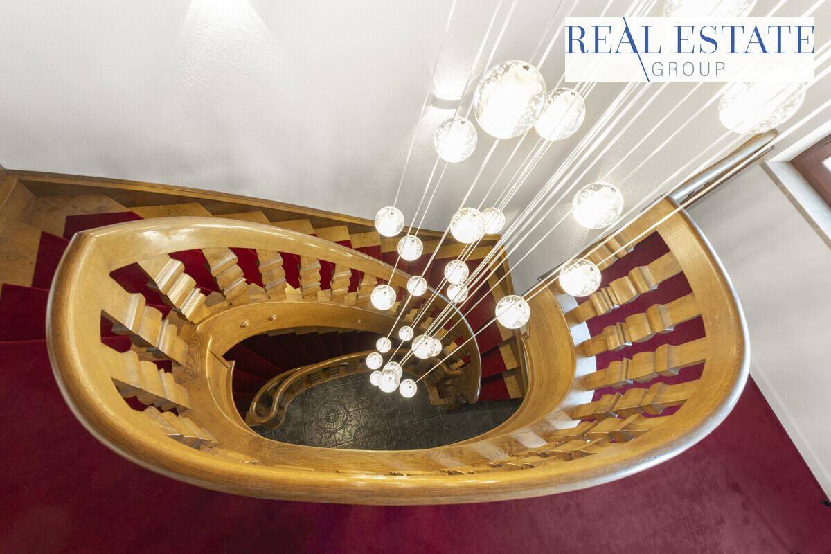 Wendeltreppe mit kunstvollem Holzgeländer und einer modernen, mehrstufigen Hängeleuchte von oben.