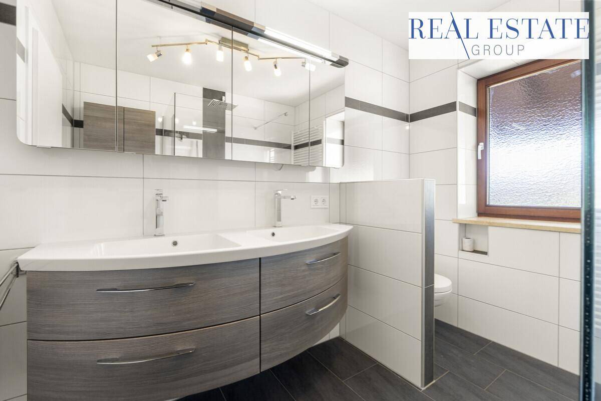 Modernes Badezimmer mit Doppelwaschbecken, Spiegelschrank und Fenster, hell gefliest.