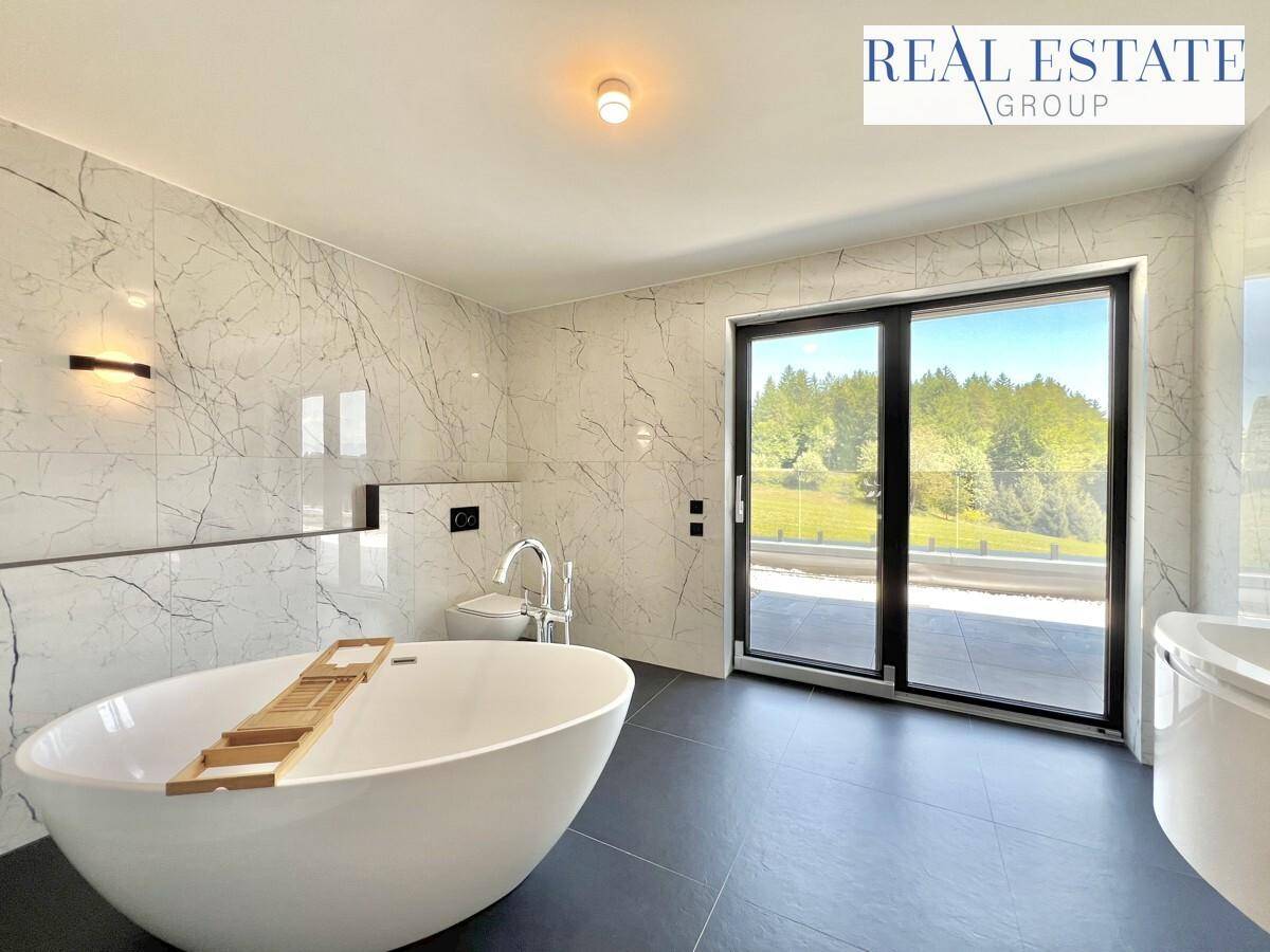 Luxuriöses Badezimmer mit freistehender Badewanne, Marmorfliesen und großen Fenstern mit Weitblick.