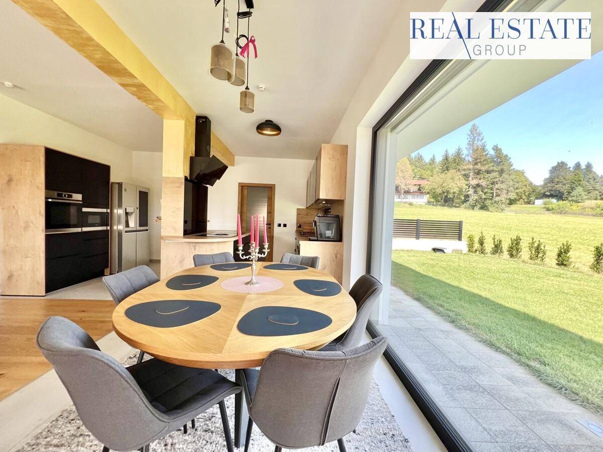 Moderner Essbereich mit Holztisch, grauen Stühlen und direktem Zugang zur Terrasse mit Gartenblick.