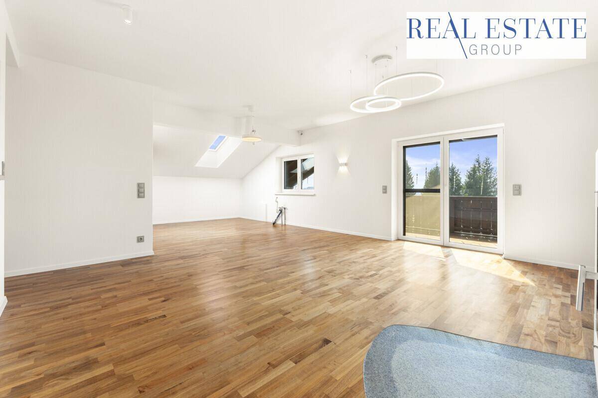 Heller, leerer Raum mit Holzboden, Dachschrägen und Zugang zu einem Balkon.