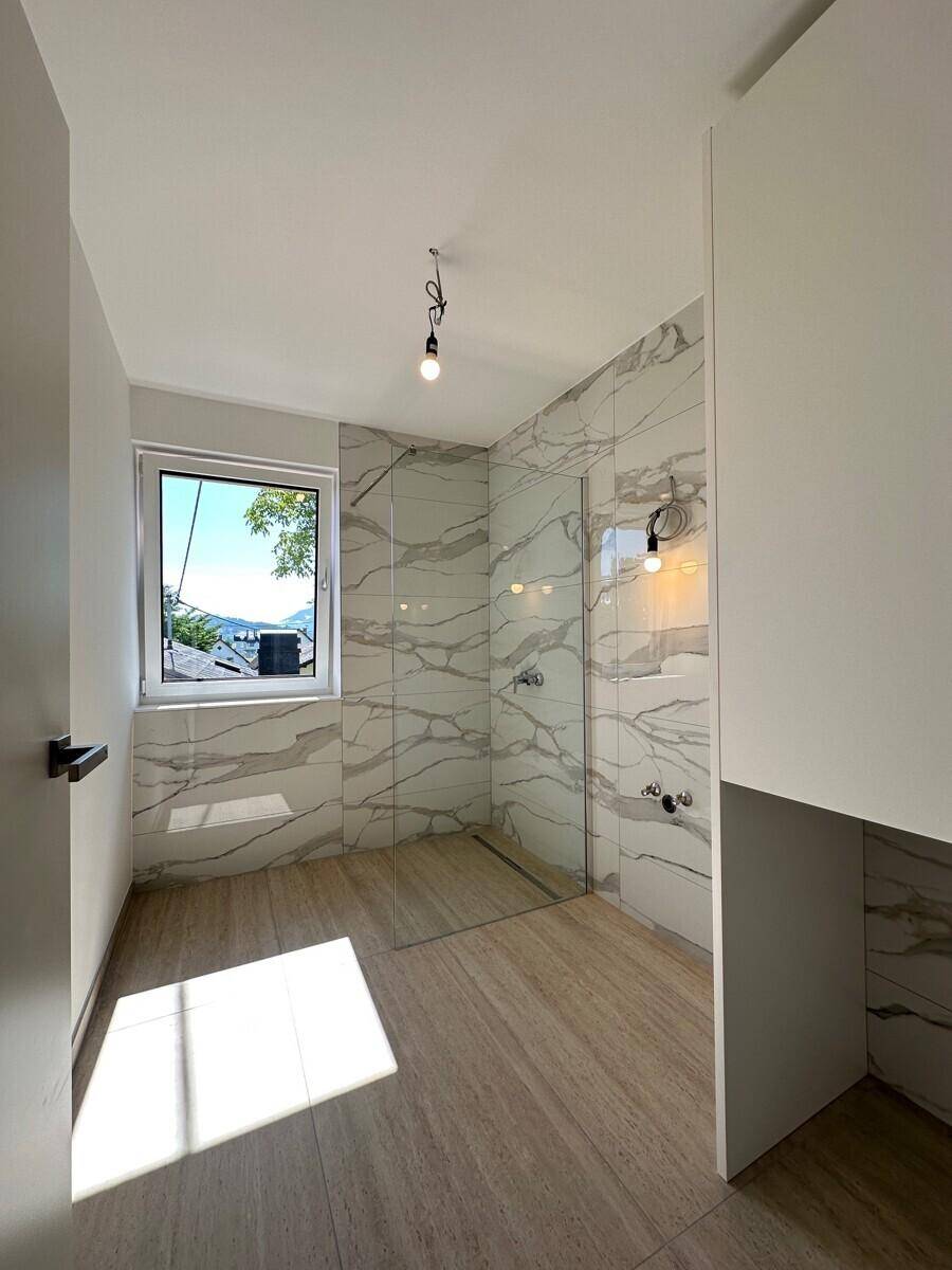 Modernes Badezimmer mit großformatigen Marmorfliesen, begehbarer Dusche und Fenster.