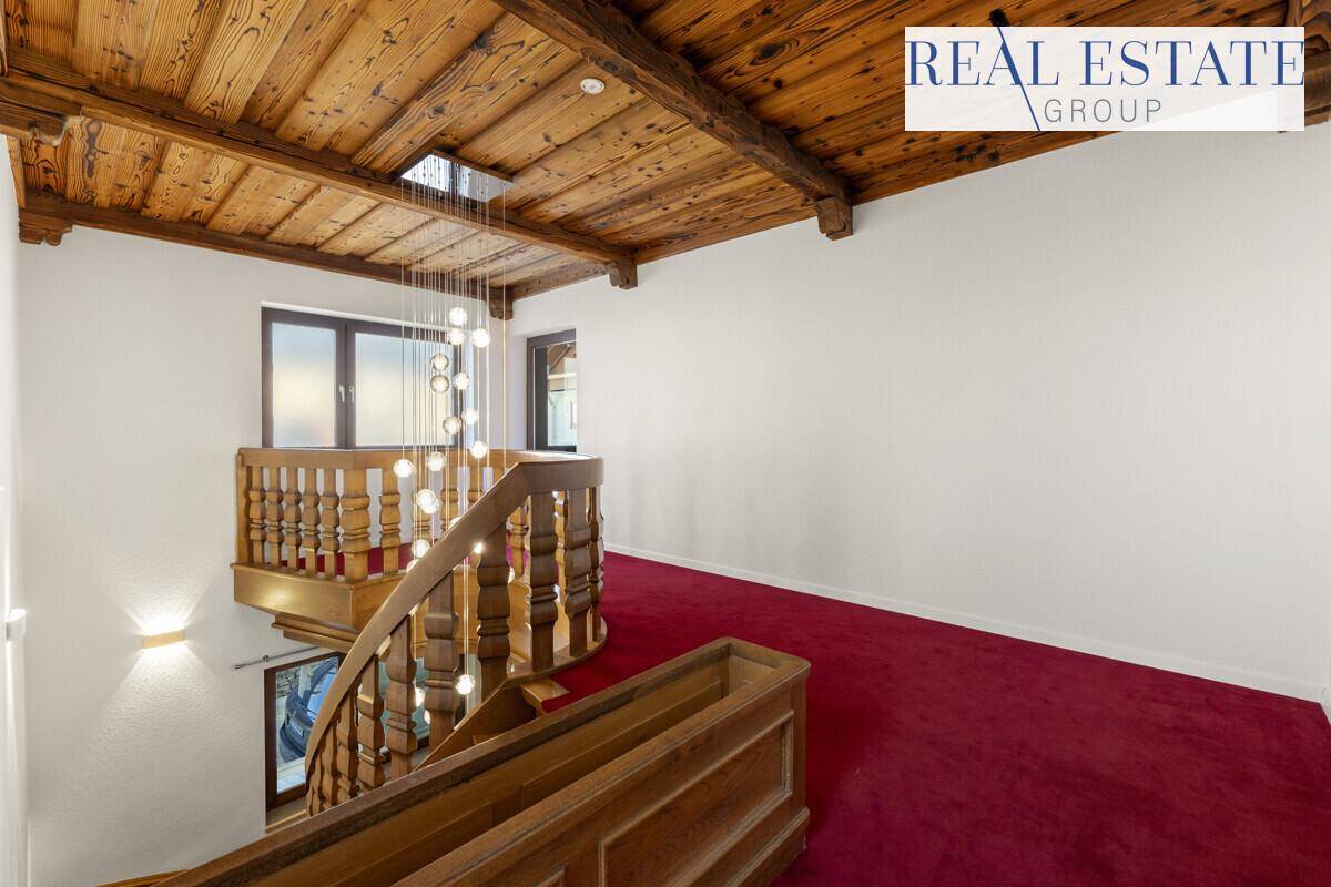 Elegantes Treppenhaus mit rotem Teppich, Holzgeländer und einer modernen Hängeleuchte.