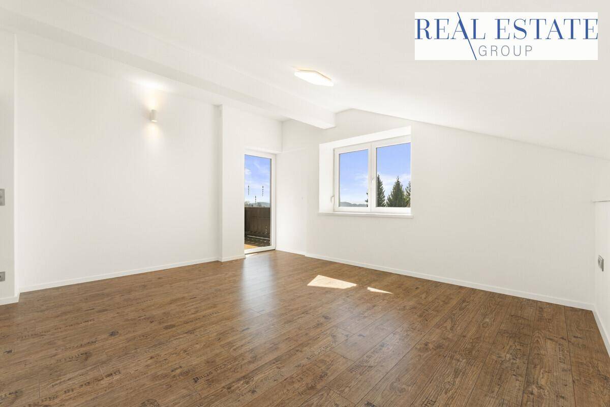 Geräumiges, leeres Schlafzimmer mit Holzboden, Dachschrägen und Zugang zu einem kleinen Balkon.