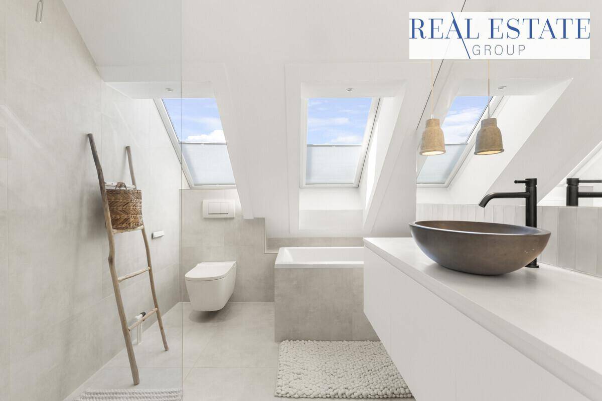 Helles Badezimmer mit Badewanne, Toilette, modernem Waschtisch und viel Tageslicht durch Dachfenster.