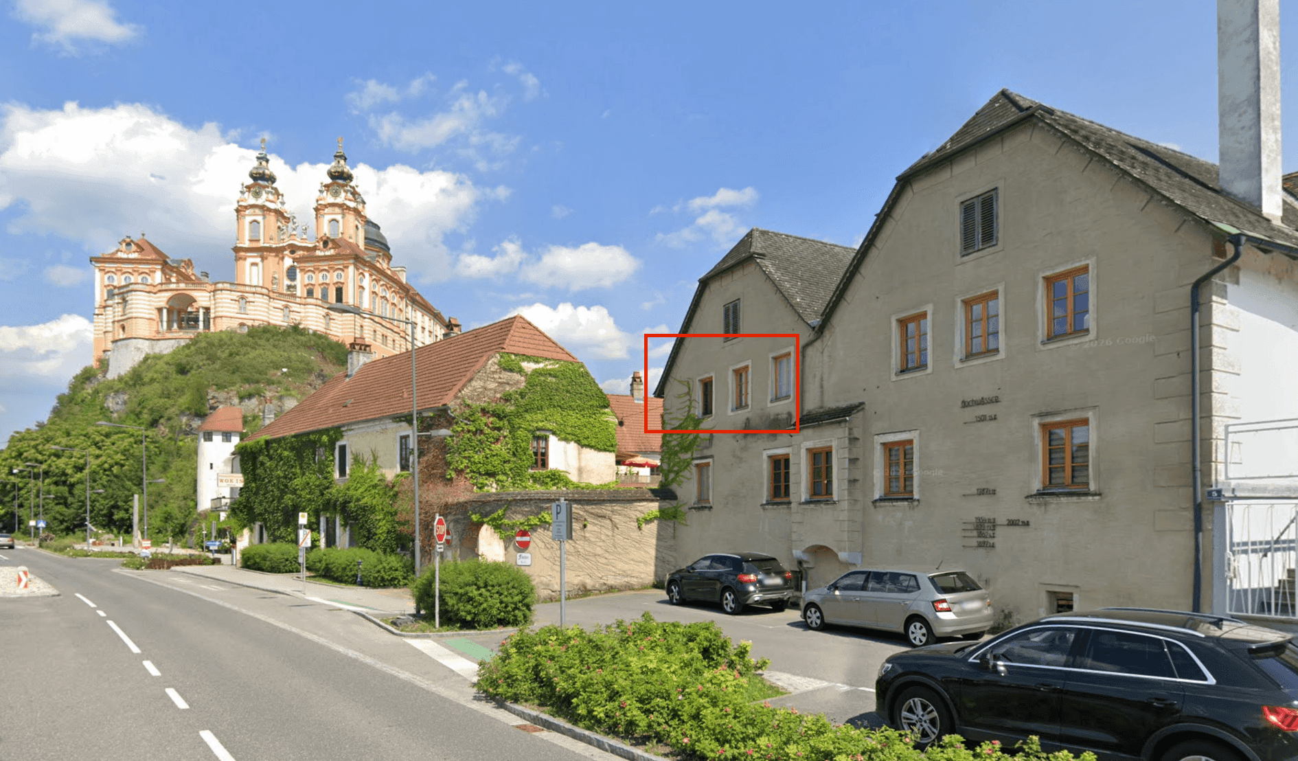 Historisches Gebäude in einer städtischen Umgebung mit Blick auf ein imposantes Kloster auf einem Hügel.