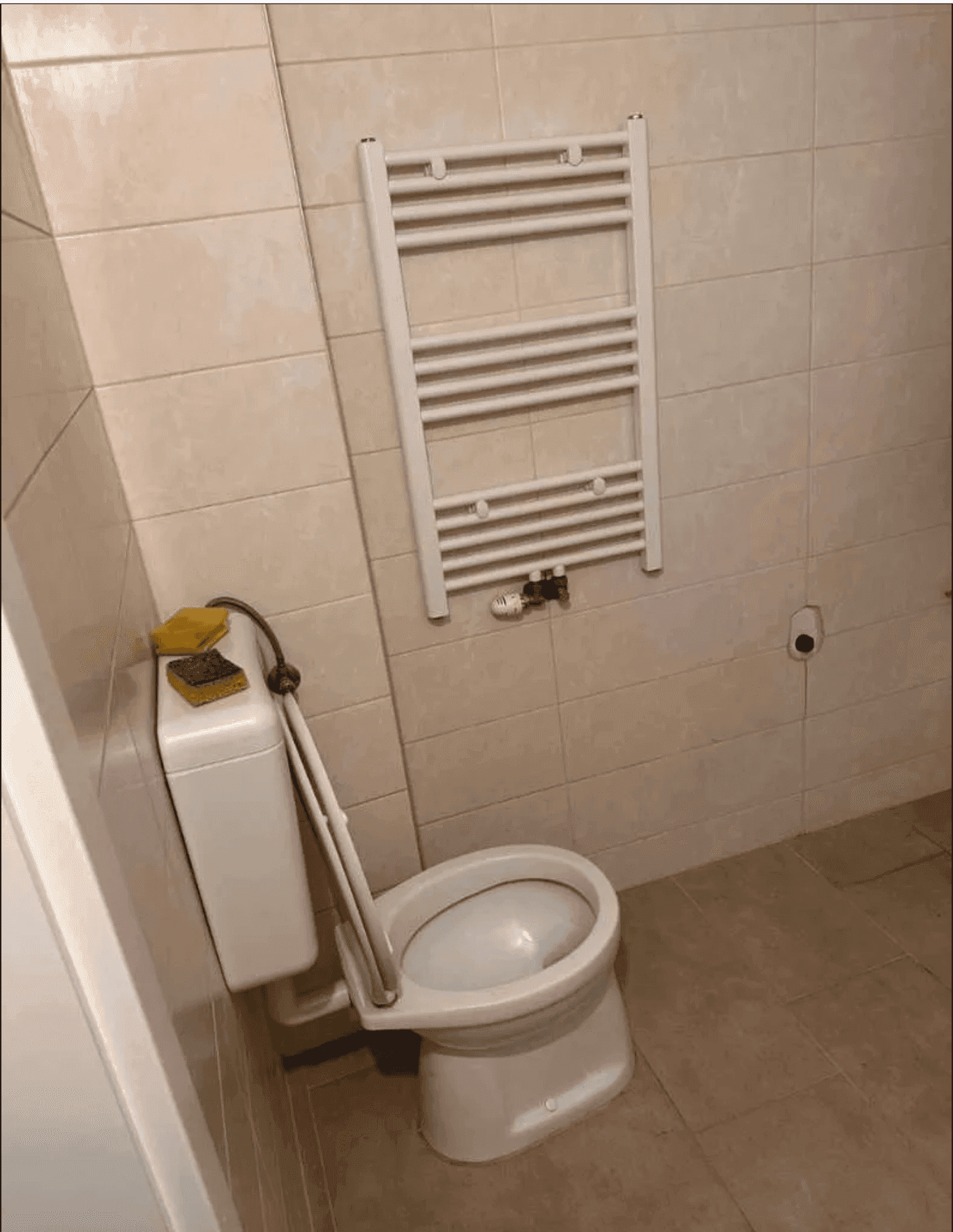 Separates WC mit Toilette, beheiztem Handtuchhalter und beigefarbenen Fliesen.