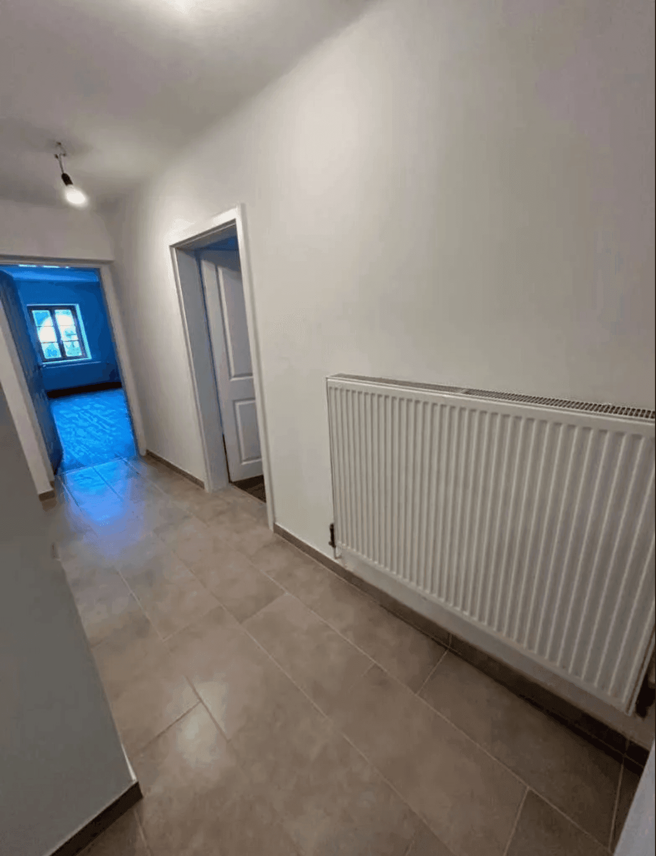 Heller Flur mit Fliesenboden und Heizkörper, der verschiedene Bereiche der Wohnung verbindet.