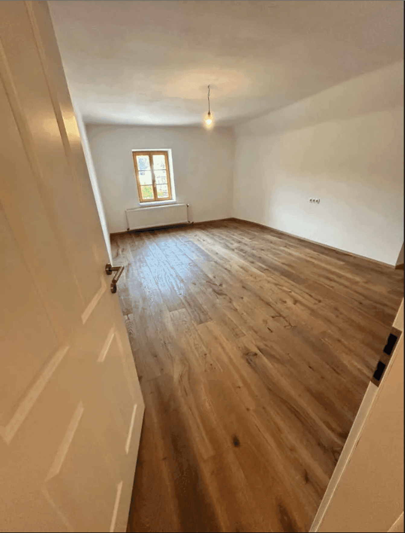 Geräumiges Zimmer mit Holzboden und einem Fenster, das viel Tageslicht hereinlässt.