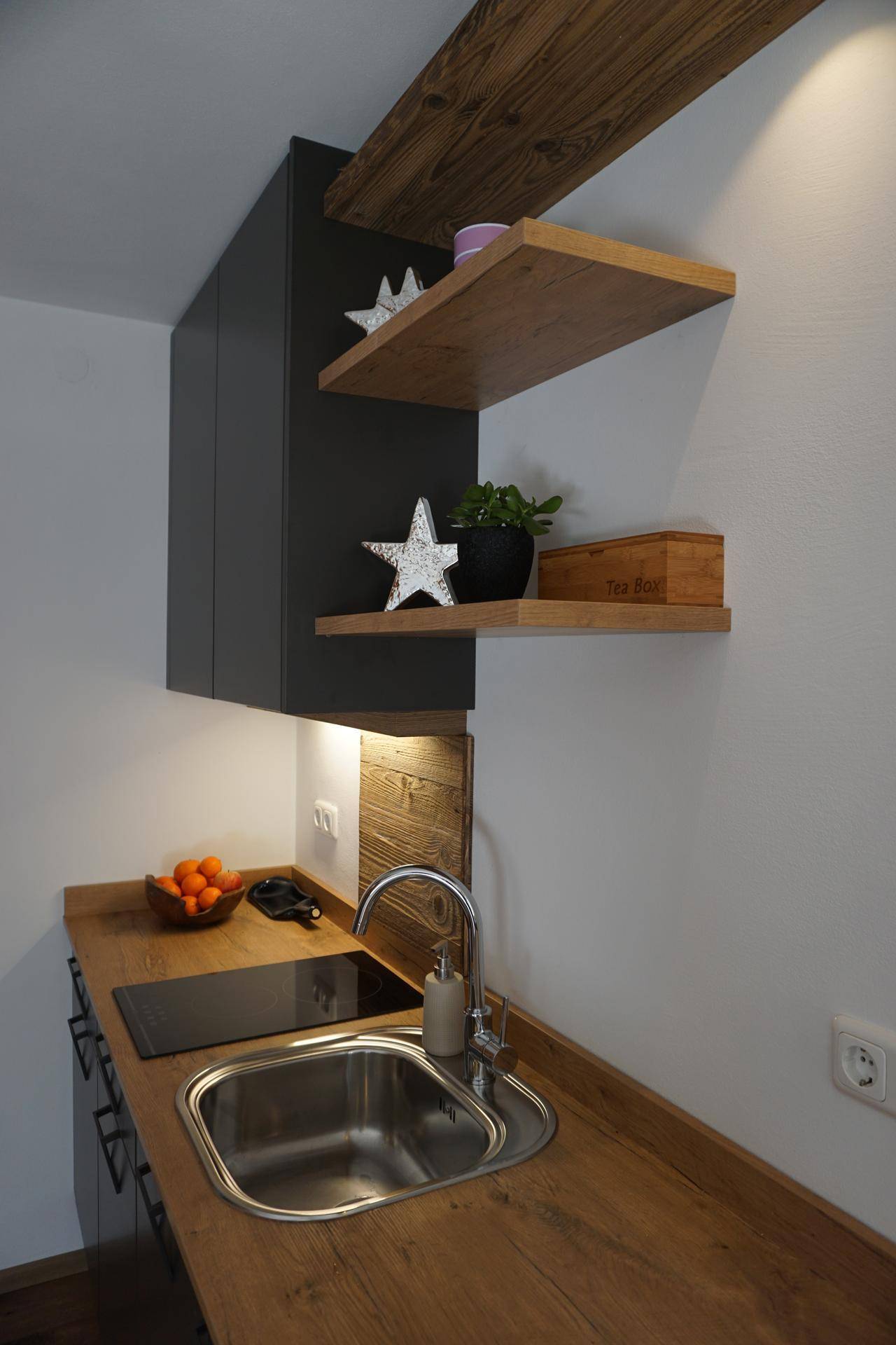 Kleine Küchenzeile mit Holz-Arbeitsplatte, Spüle, Induktionskochfeld und modernen Hängeschränken.