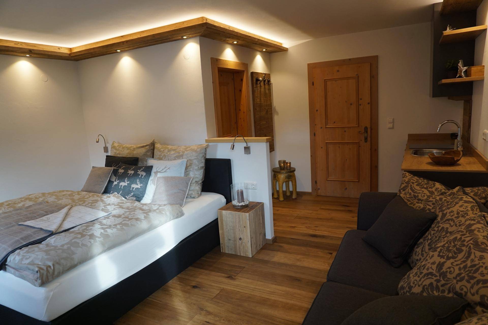Helles Studio-Apartment mit Doppelbett, Sofa, Holzboden und integrierter Küchenzeile.