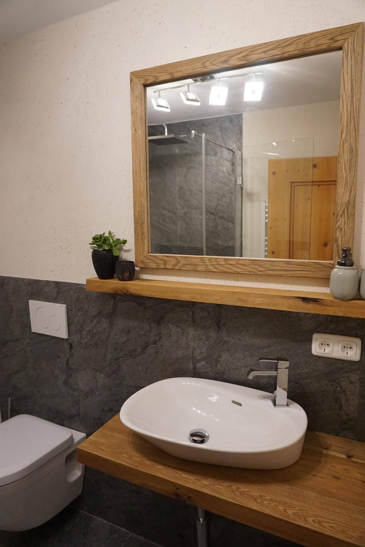 Modernes Badezimmer mit Holzwaschtisch, großem Spiegel und einer begehbaren Dusche im Hintergrund.