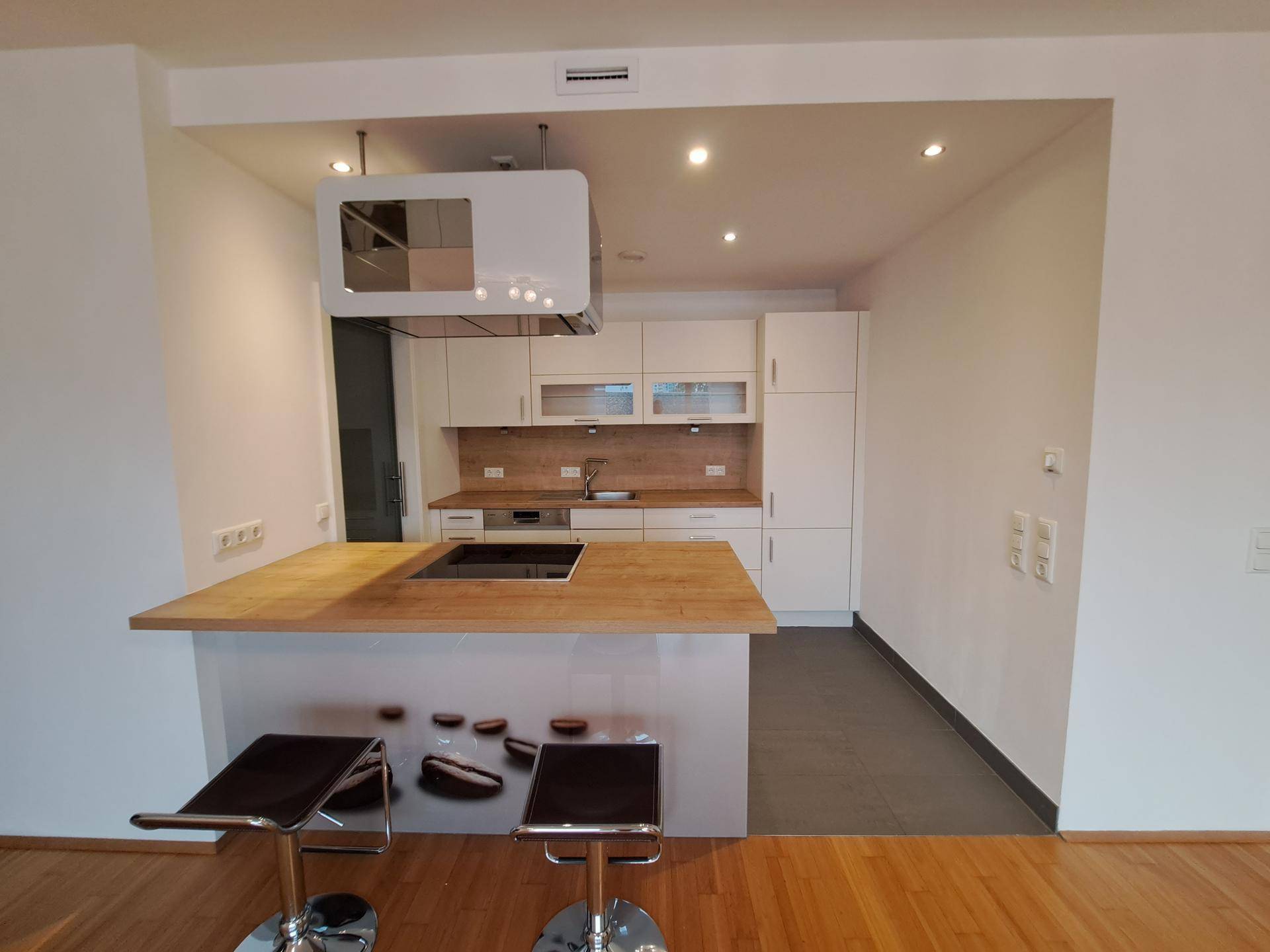 Moderne Einbauküche mit Kochinsel, Induktionskochfeld und hellen Holz-Arbeitsplatten.