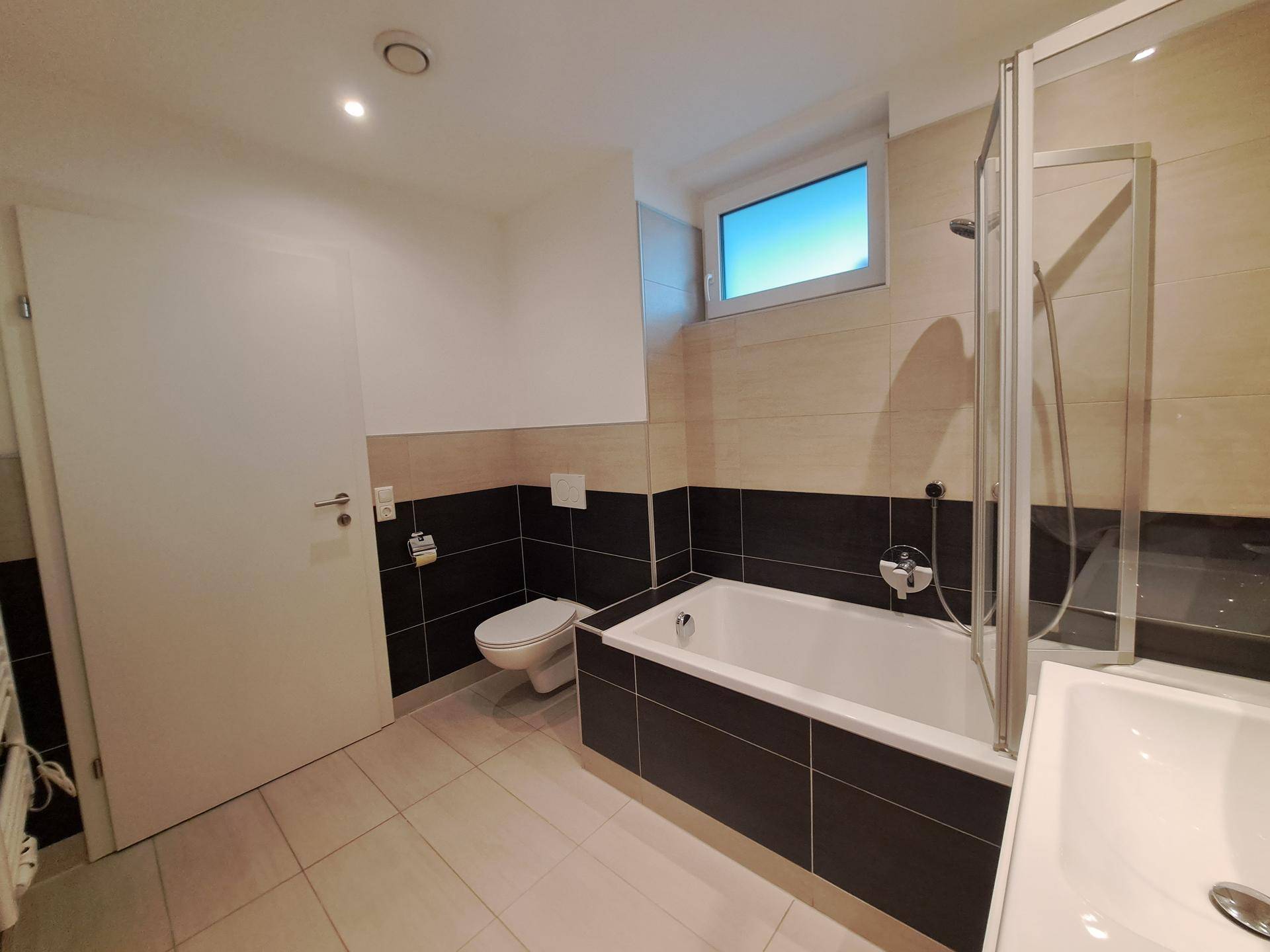 Badezimmer mit Badewanne, Dusche, WC und Fenster für natürliche Belüftung und Licht.