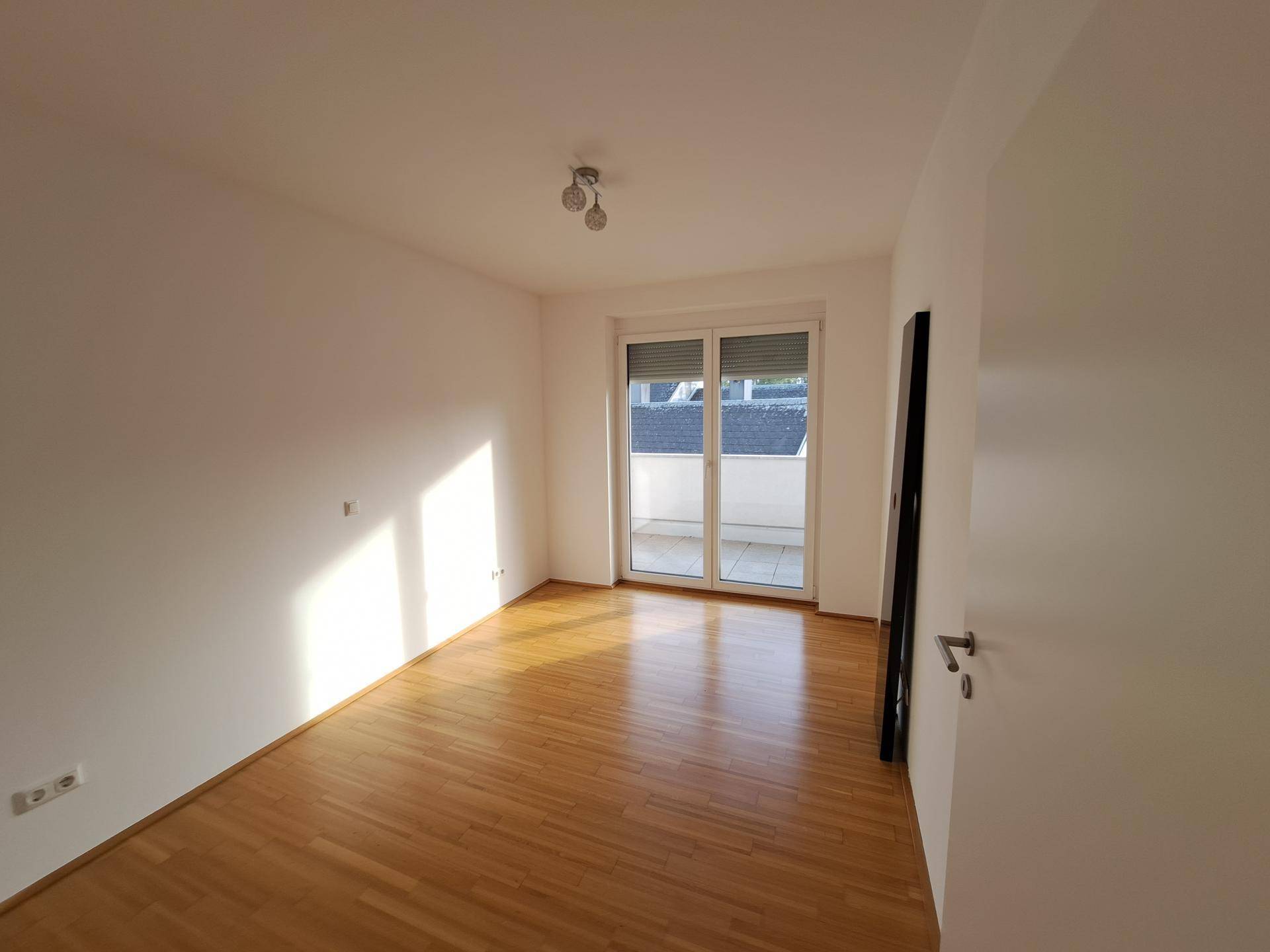 Helles Zimmer mit Parkettboden und direktem Zugang zu einem Außenbereich, ideal als Schlafzimmer.