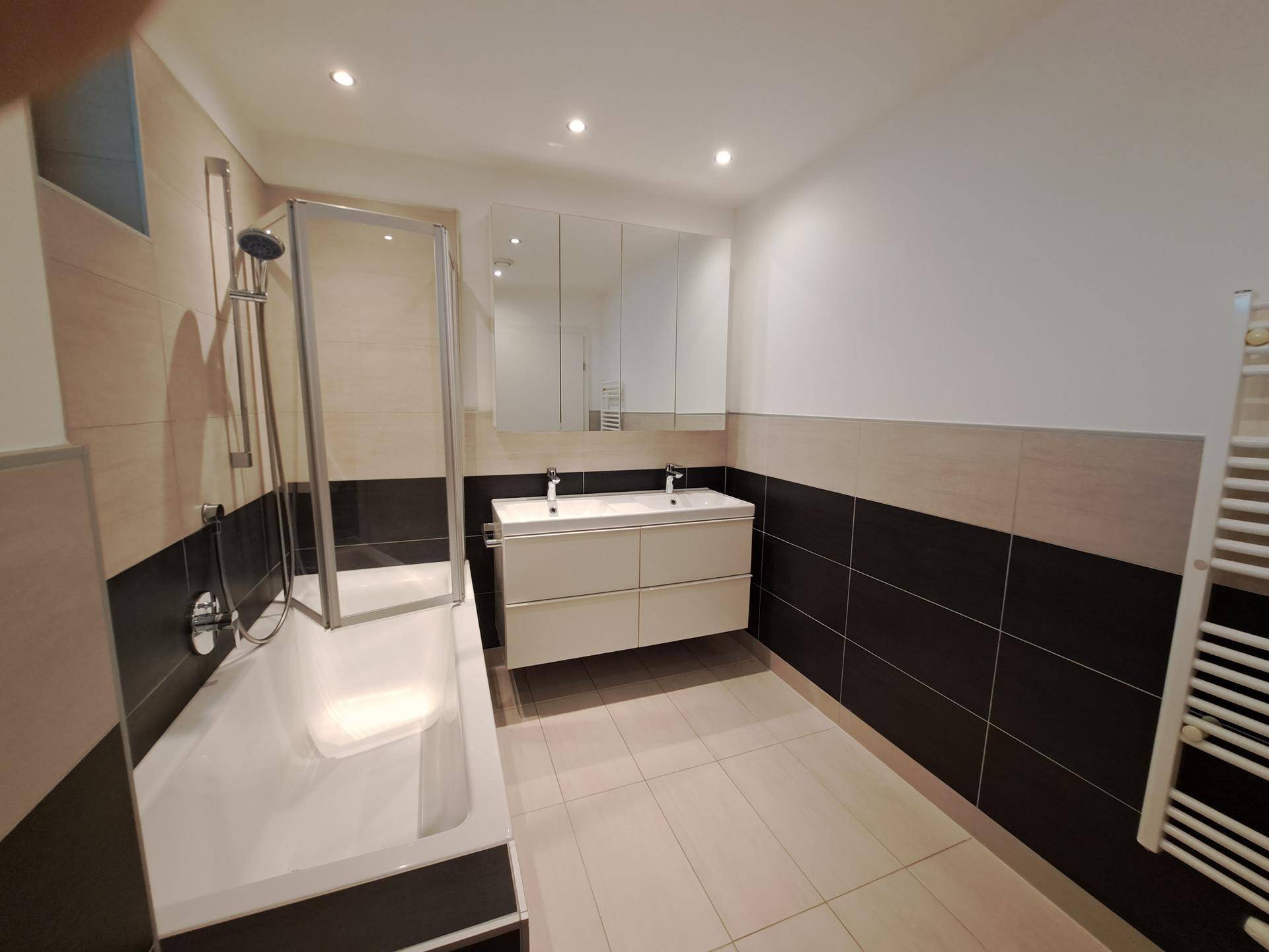 Modernes Badezimmer mit Doppelwaschbecken, Badewanne mit Duschabtrennung und Handtuchheizkörper.