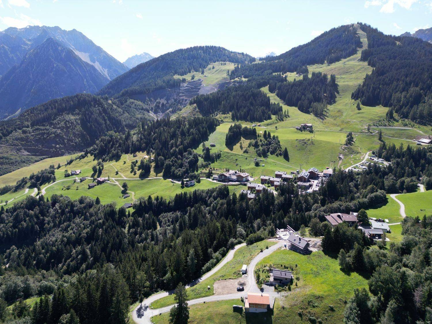 Luftaufnahme eines grünen Bergtals mit einem malerischen Dorf und gewundenen Straßen.