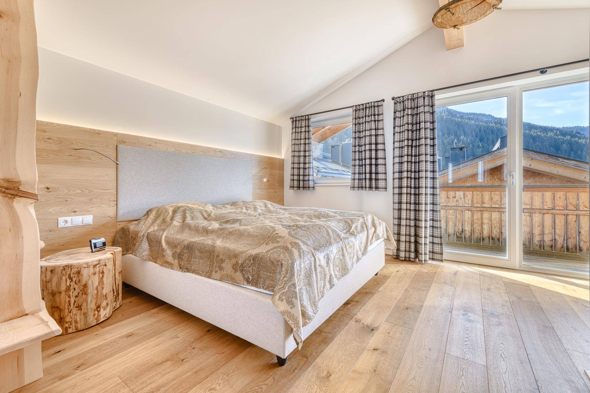 Gemütliches Schlafzimmer mit Holzboden, Dachschräge und Zugang zu einem Balkon mit Bergblick.