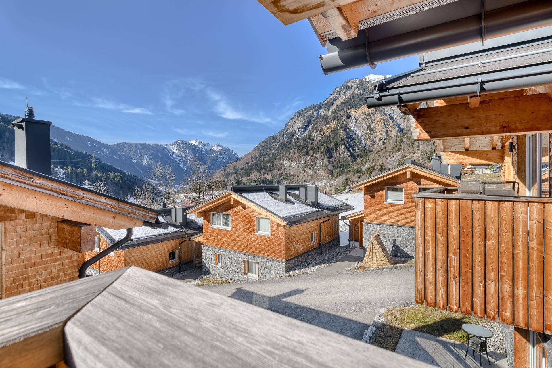Mehrere moderne Chalets mit Holzbalkonen und Steinfassaden in einer sonnigen Berglandschaft.