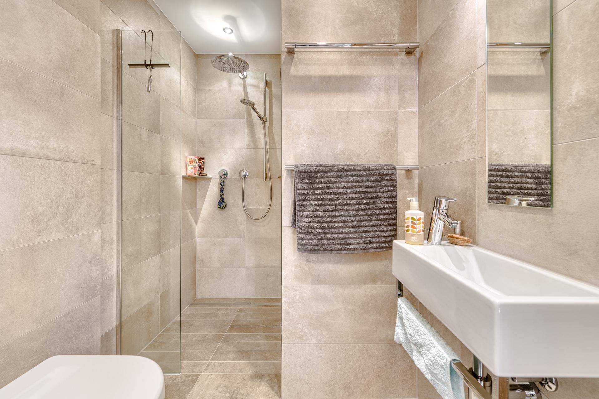 Modernes Badezimmer mit begehbarer Dusche, beigefarbenen Fliesen und einem eleganten Waschbecken.