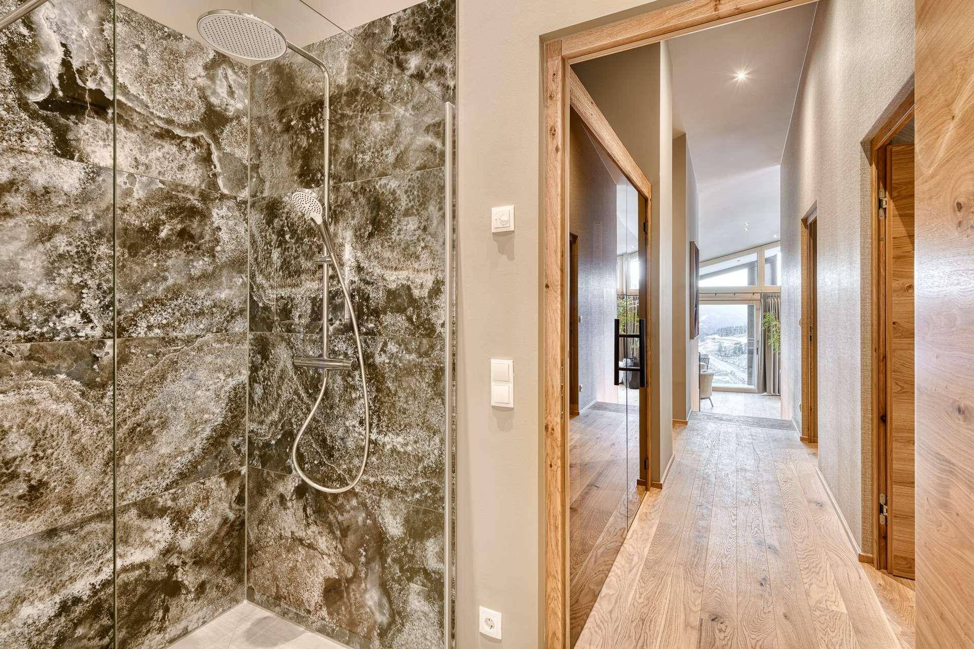 Modernes Badezimmer mit begehbarer Dusche und Natursteinfliesen, angrenzend an einen Flur.