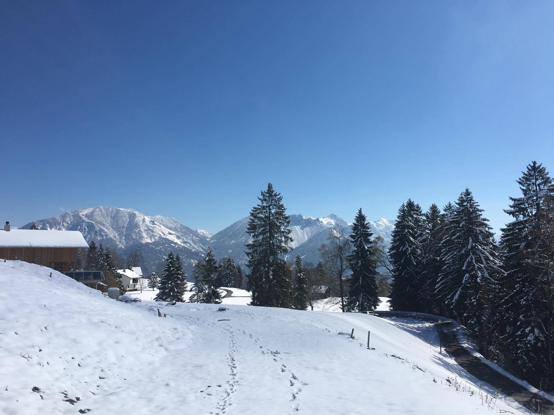 Ruhige, schneebedeckte Landschaft mit vereinzelten Häusern und einer Bergkulisse in der Ferne.
