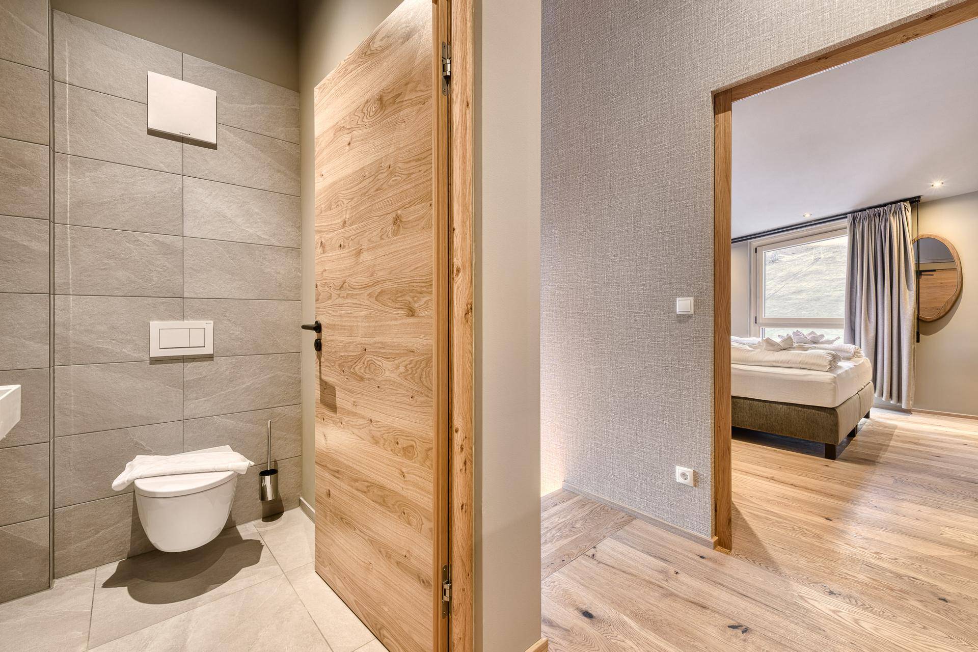 Modernes Gäste-WC mit Wand-WC und grauen Fliesen, angrenzend an ein Schlafzimmer.